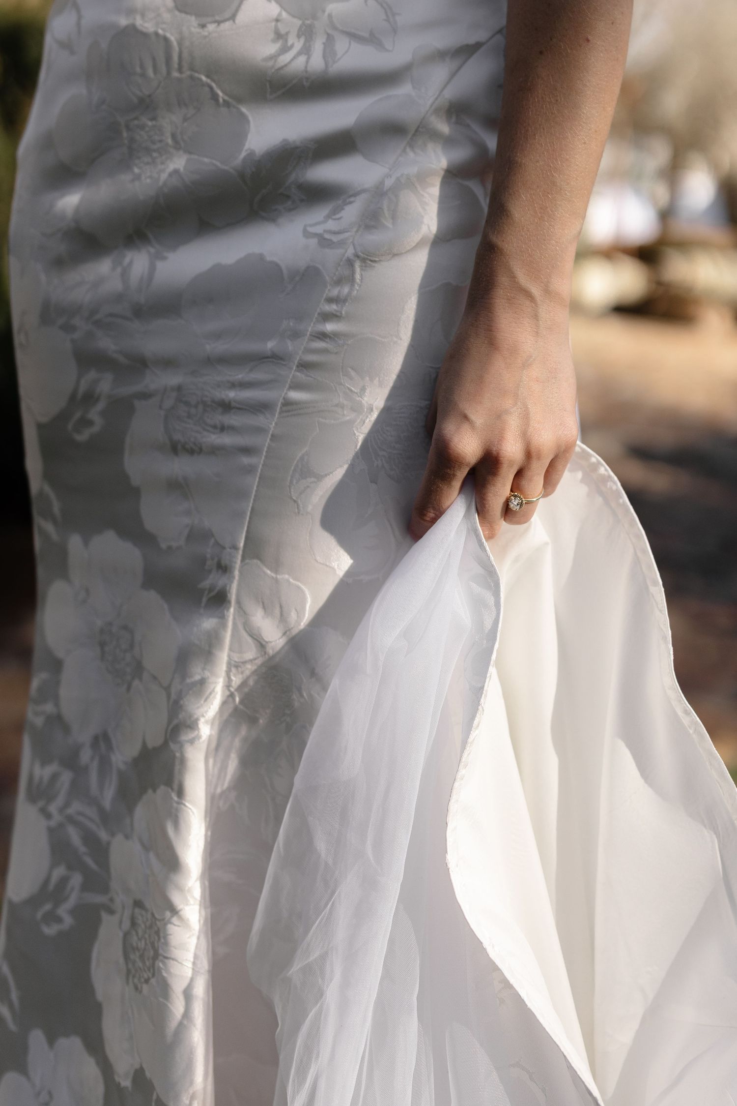 Close-up details of a white wedding dress with delicate lace patterns and tulle fabric flowing in natural light.