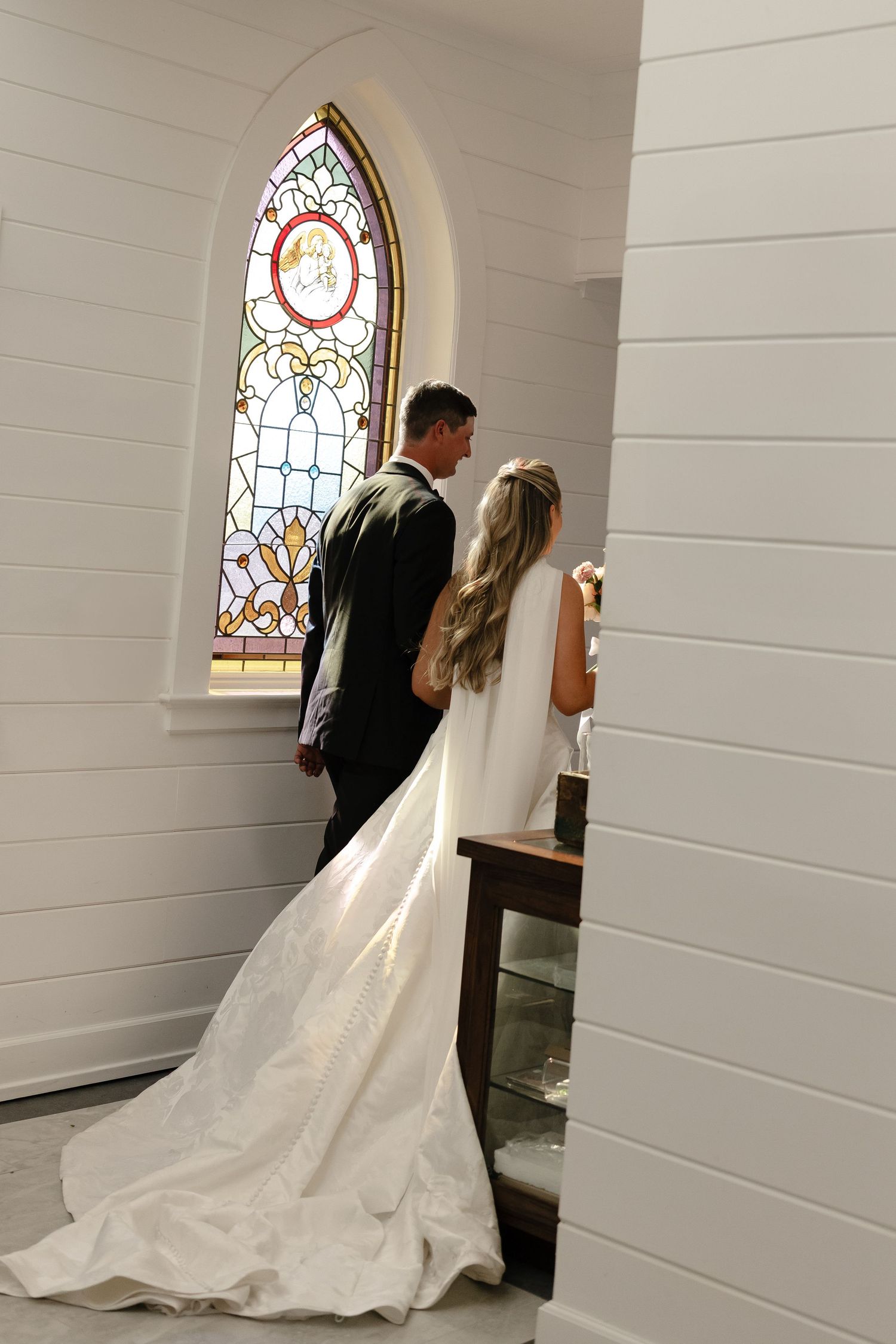 A couple stands before a beautiful stained glass church window during their wedding ceremony.