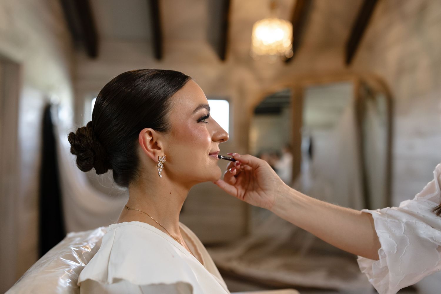 A bride in a white dress gets her hair styled in an elegant updo at a luxurious salon.