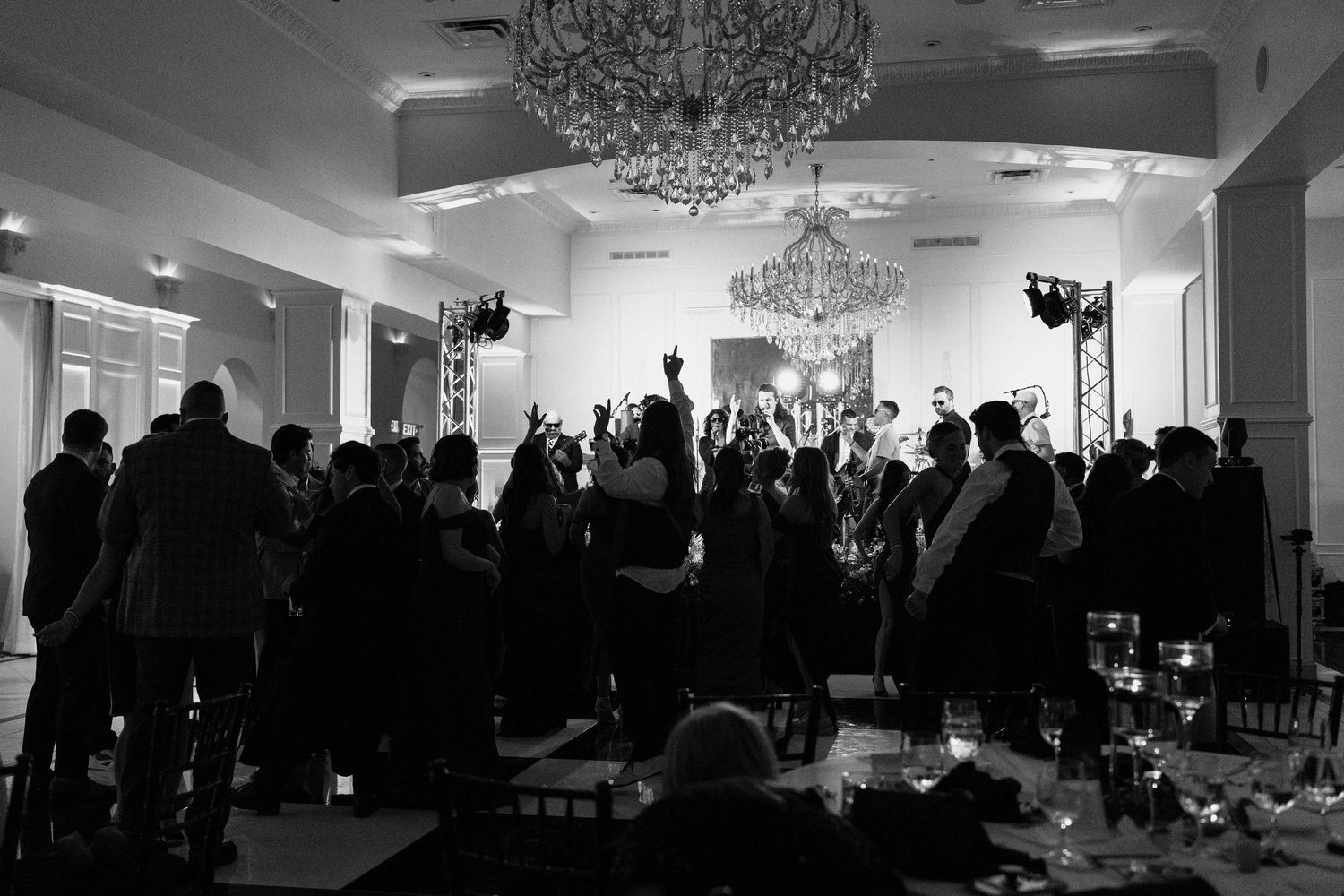 A large group of silhouetted people gathered in a dimly lit banquet hall with elegant crystal chandeliers overhead.