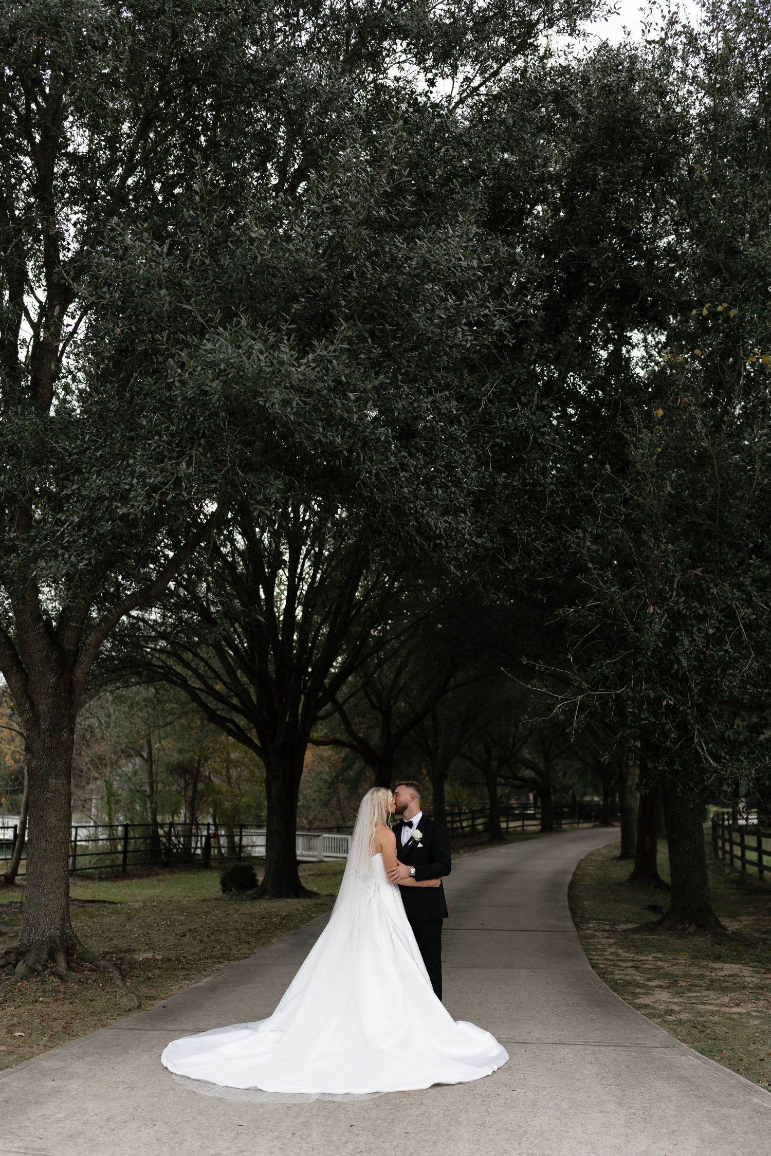 A couple shares an intimate moment on a tree-lined path during their wedding photoshoot.