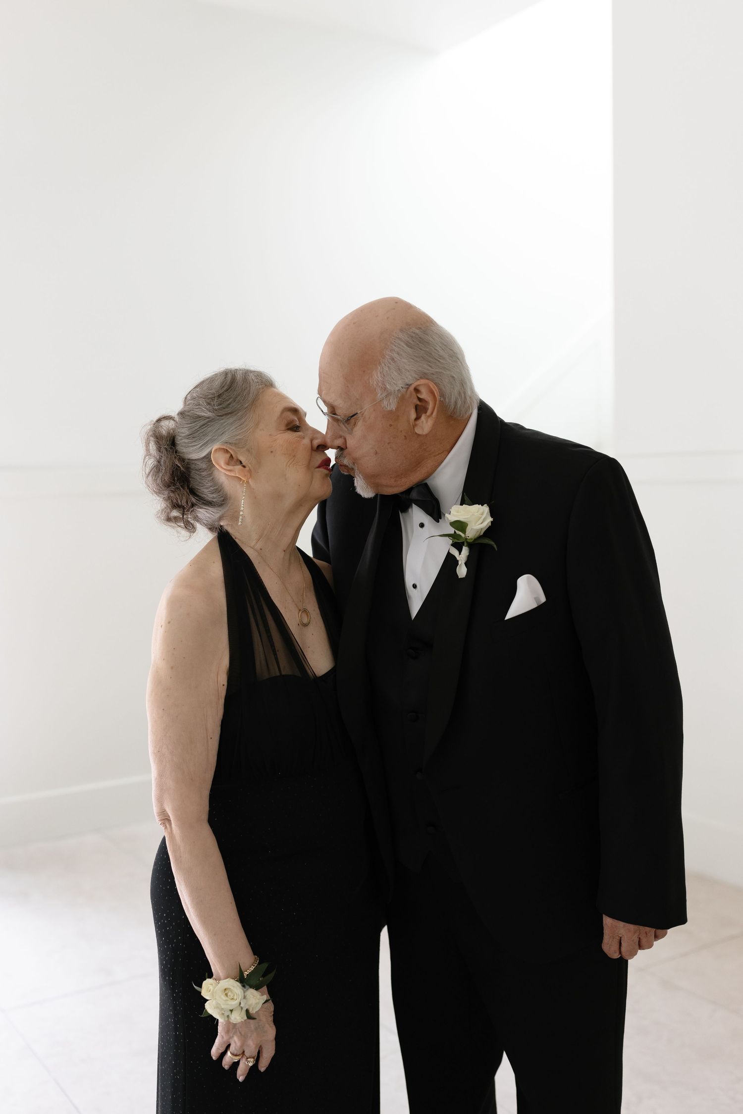 An elegant couple in formal black attire share an intimate moment during a special occasion.