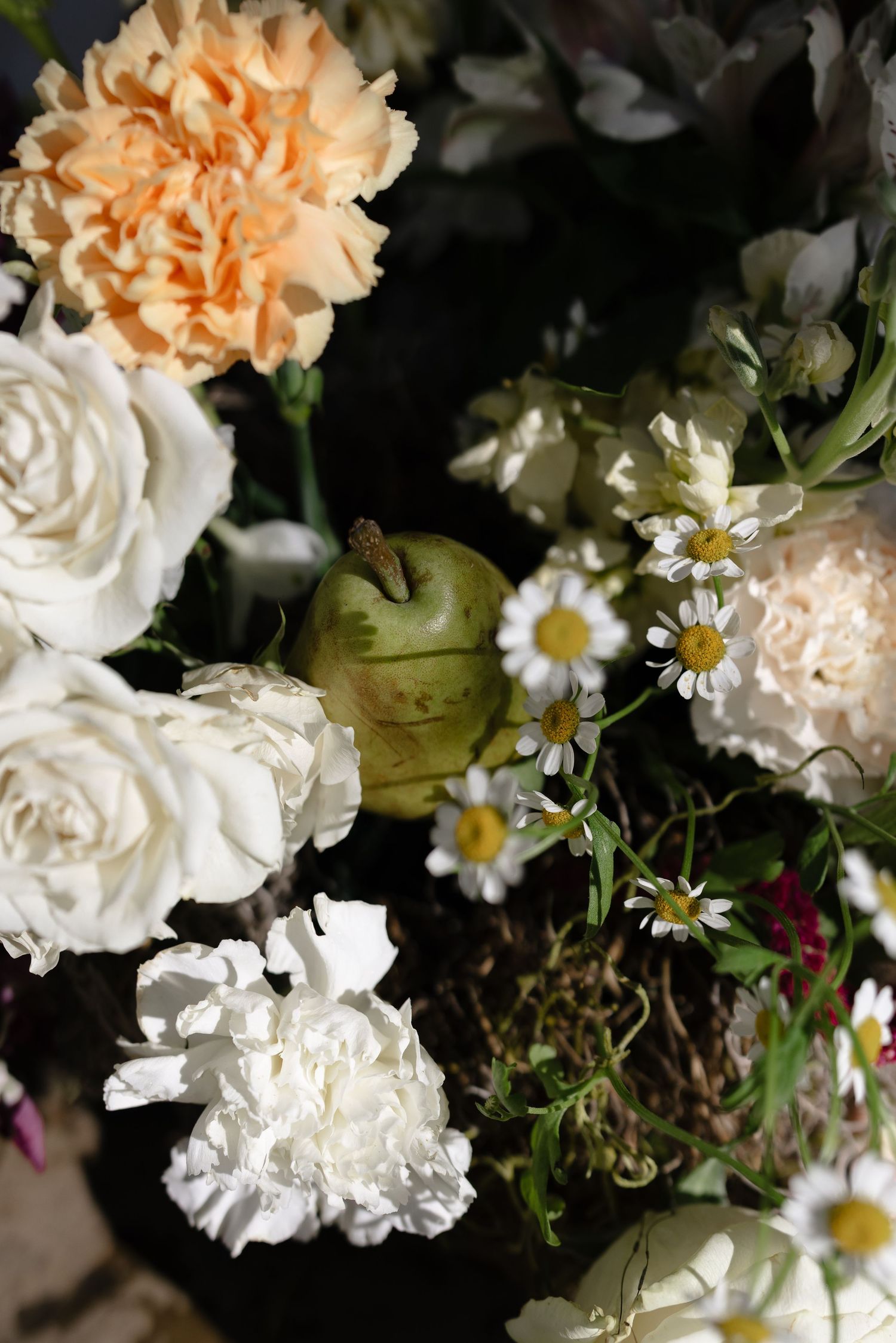 A close-up view of white and peach-colored carnations with small daisies in a floral arrangement against a dark background.