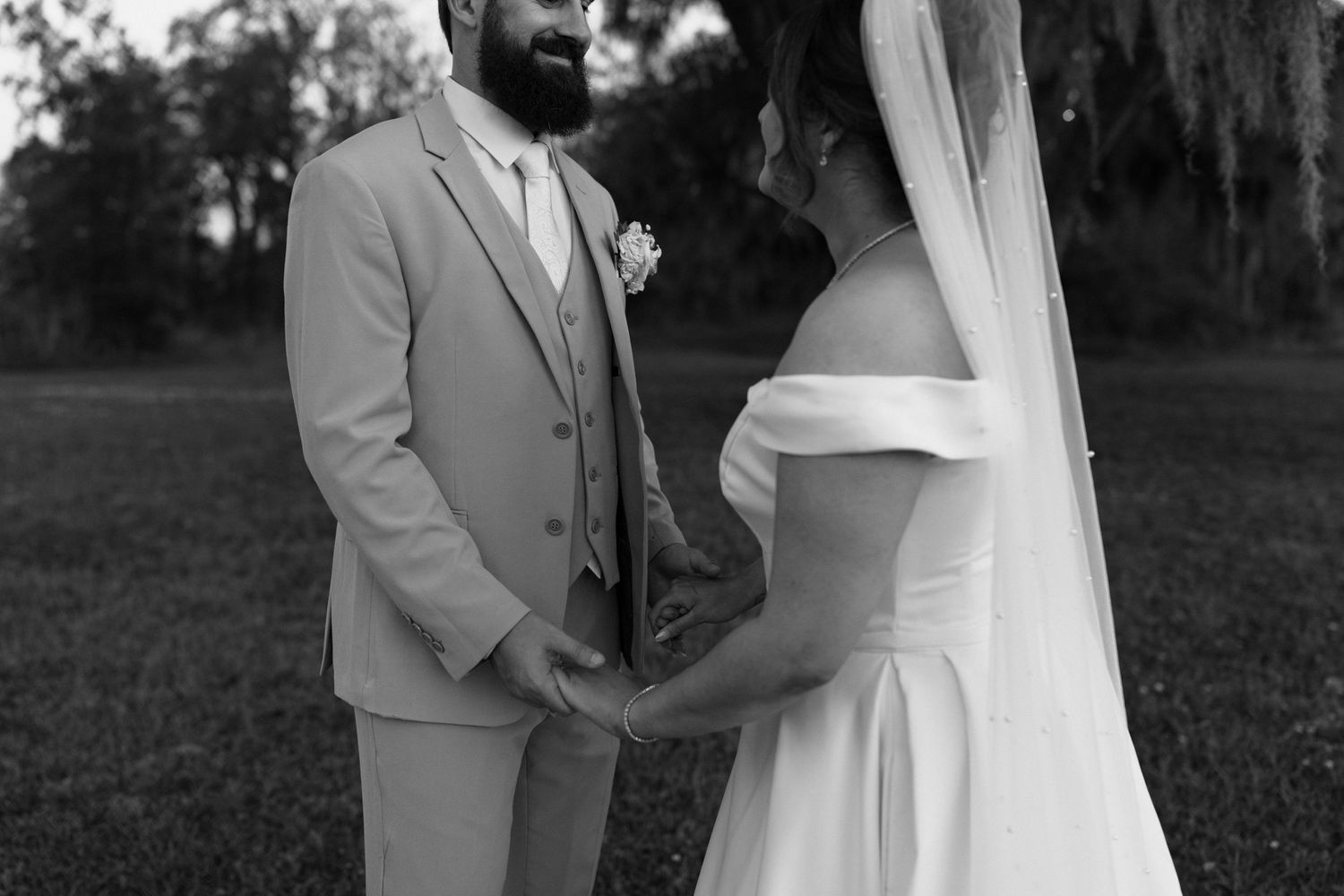 A black and white wedding photo showing a couple holding hands outdoors with Spanish moss trees in the background.