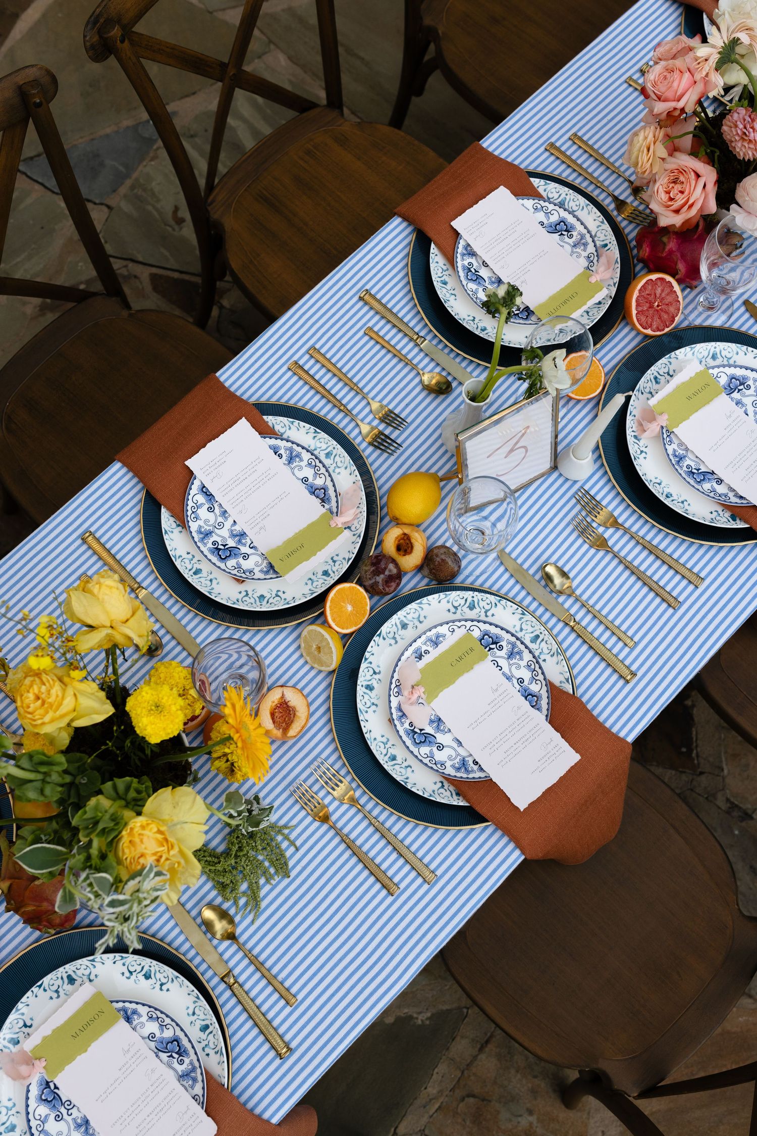 Elegant table setting with blue striped runner, white and blue china plates, and bright yellow floral centerpieces.
