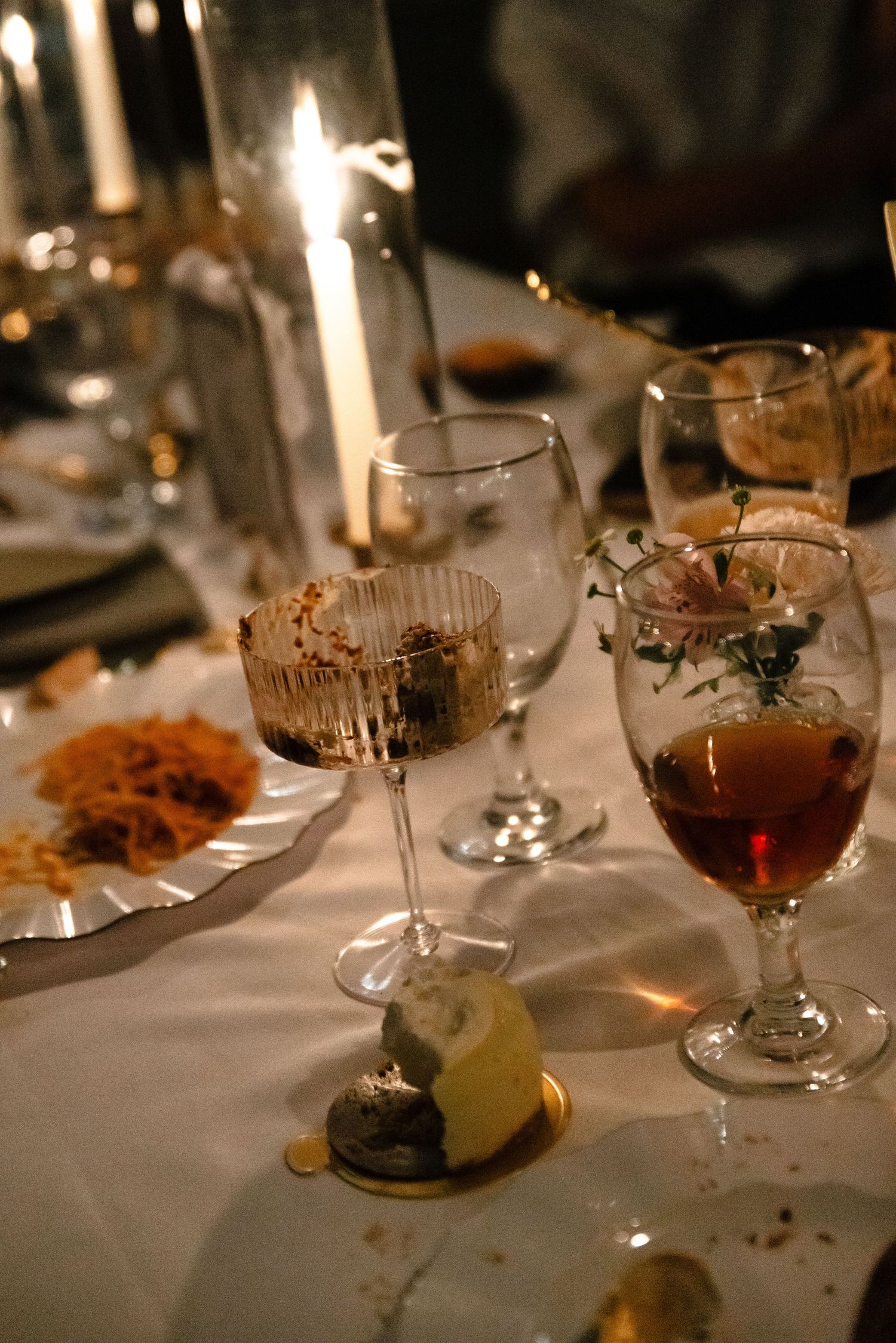 Elegant dining table setting with lit candles, wine glasses, and white tablecloth in warm ambient lighting.