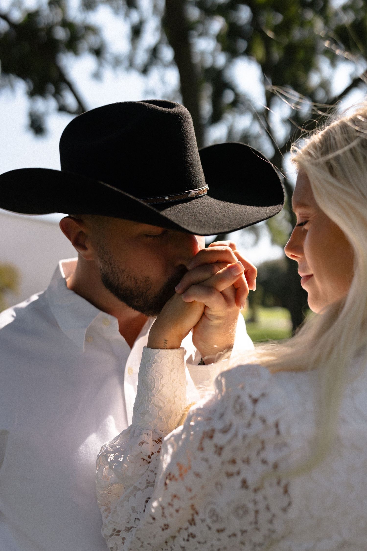 A romantic couple in baseball caps sharing an intimate moment in sunlit outdoor setting.