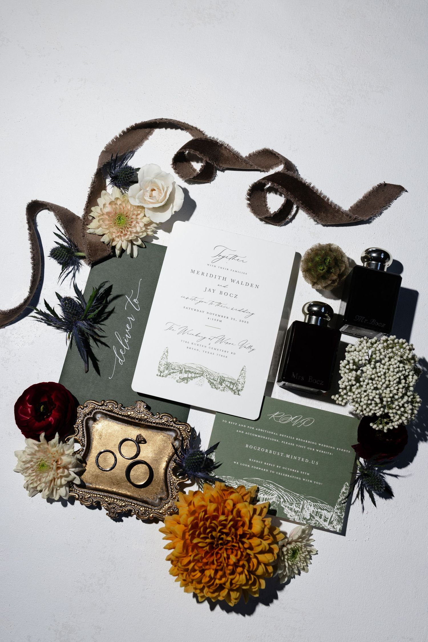 Wedding invitation suite flatlay with sage green stationery, orange marigolds, baby's breath flowers, and black ribbons.