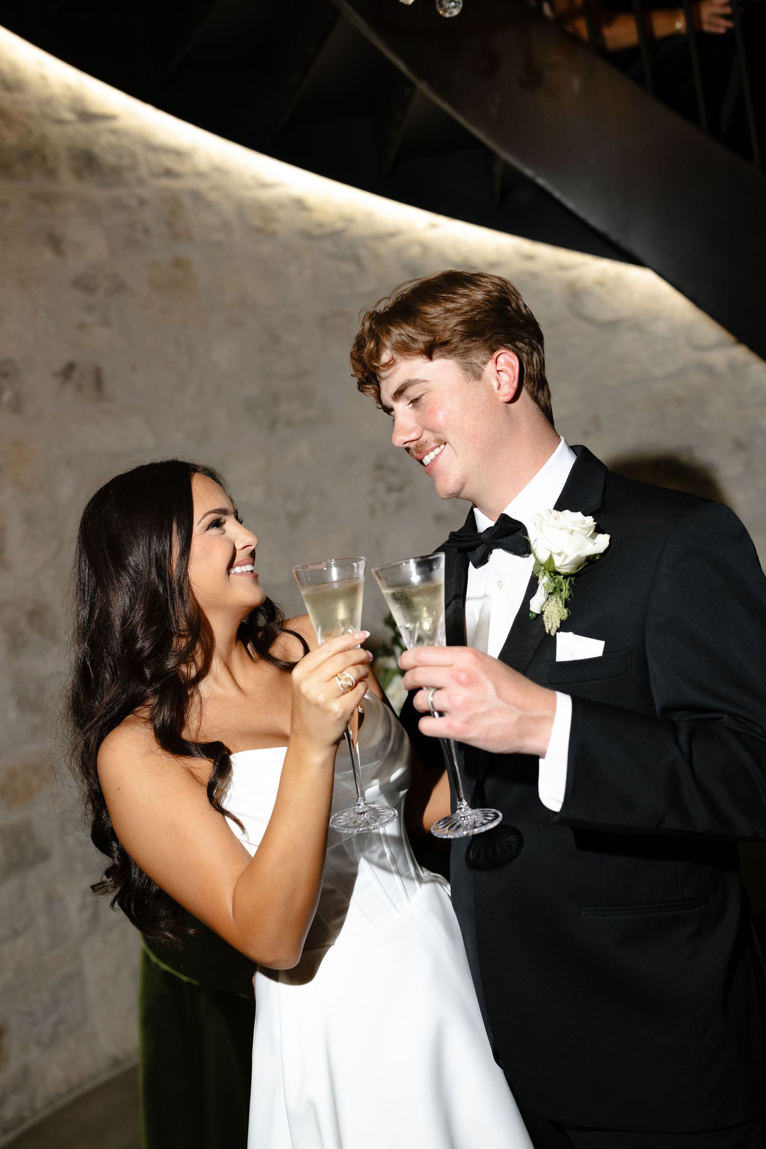 A bride and groom share a playful moment while drinking champagne together at their wedding reception.