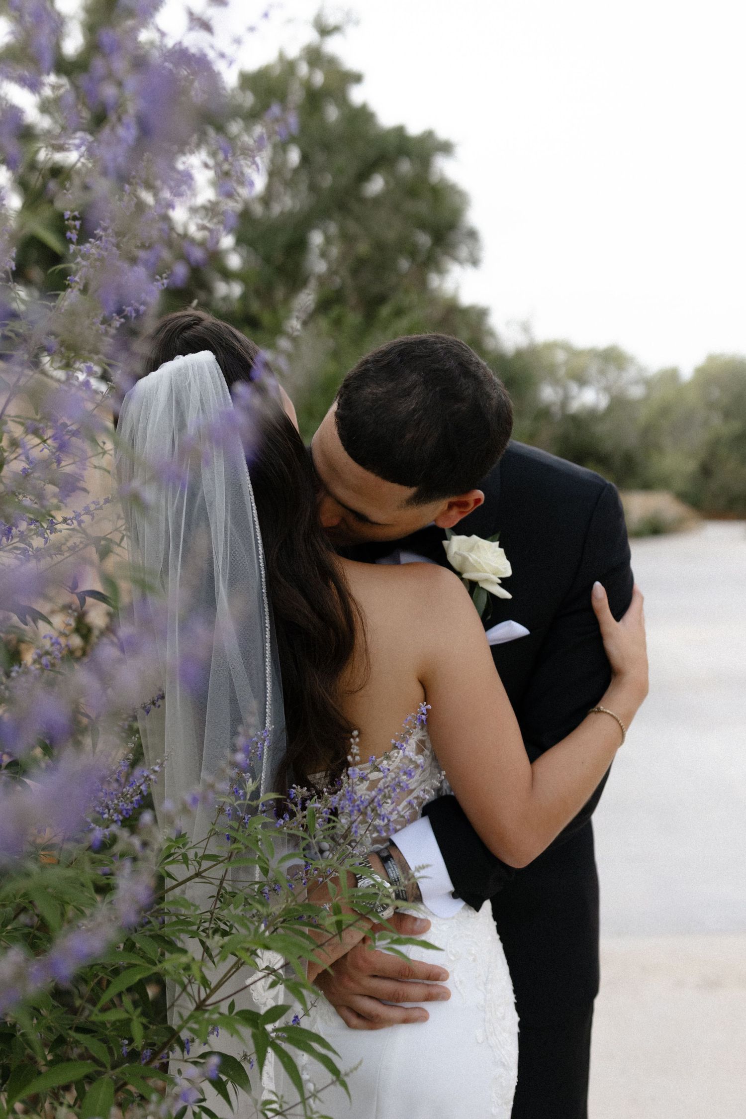 Romantic moment captured between newlyweds near blooming purple flowers outdoors.