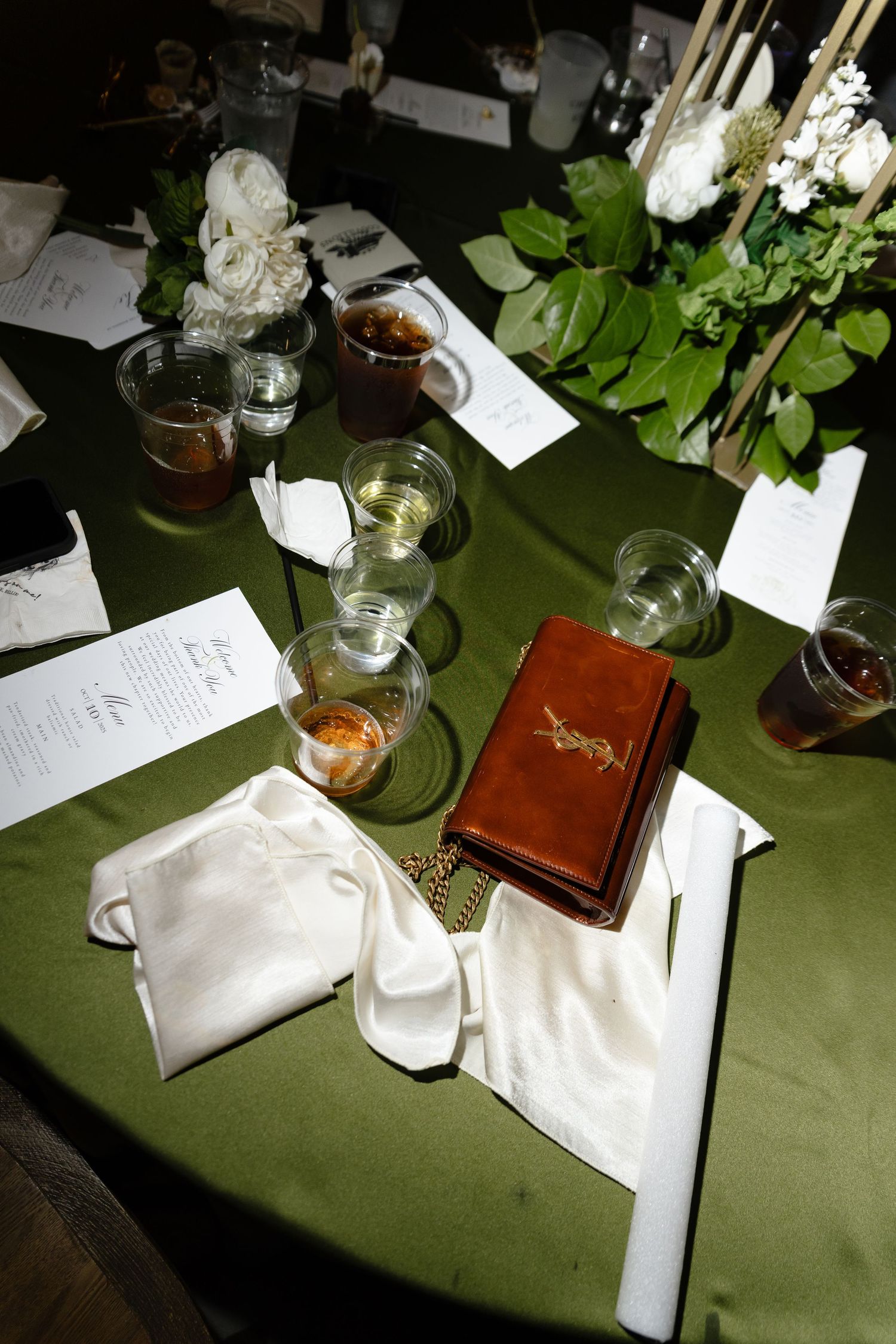 A table set for dinner with drinks, menus, and white flowers on a green tablecloth.