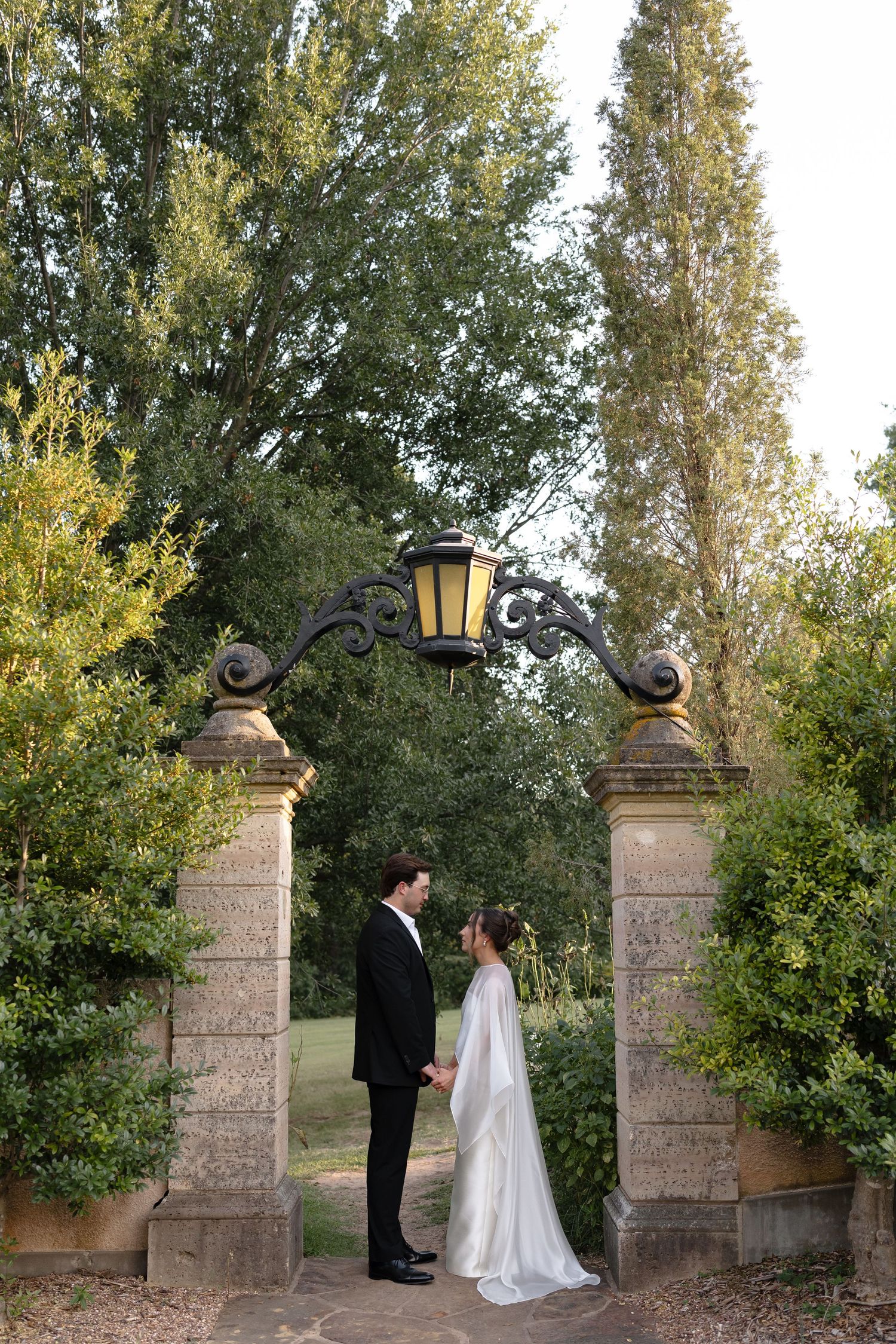 A romantic wedding scene at sunset by stone pillars and lanterns in a garden setting.