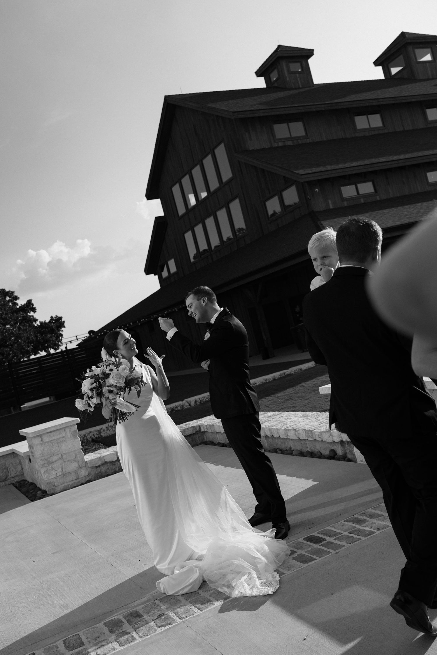 A couple in formal wedding attire dances together on an outdoor terrace in black and white photography.