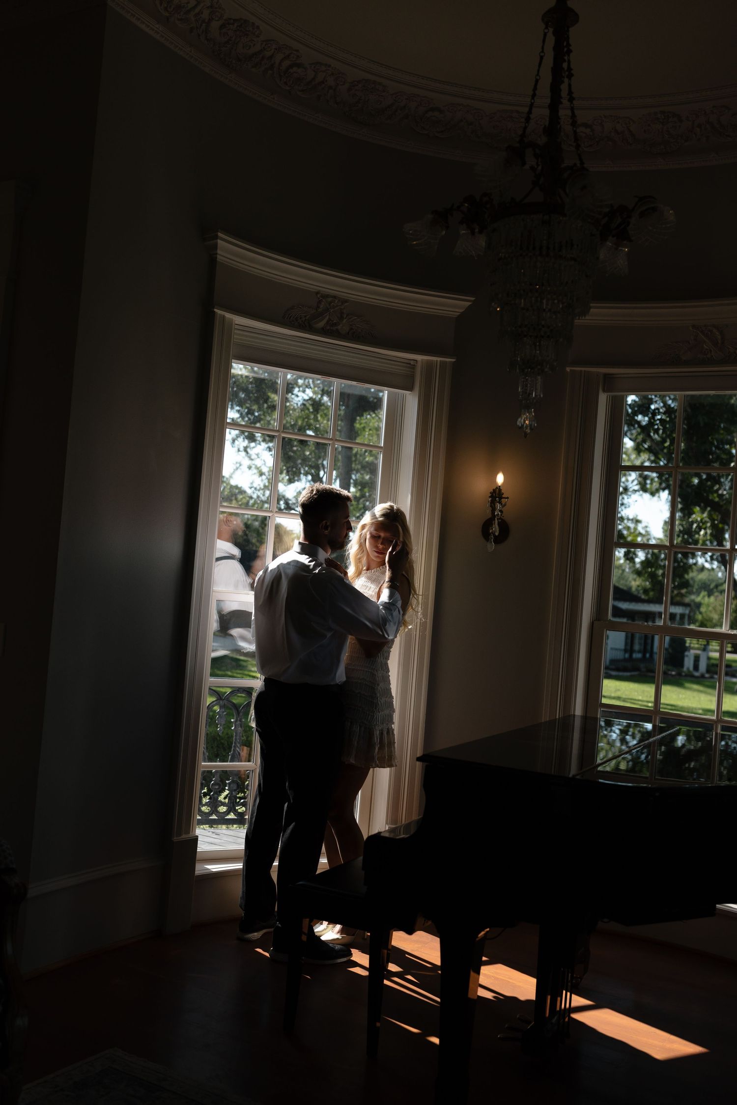 Two silhouettes dance together in a sunlit room with large windows casting dramatic shadows on the floor.