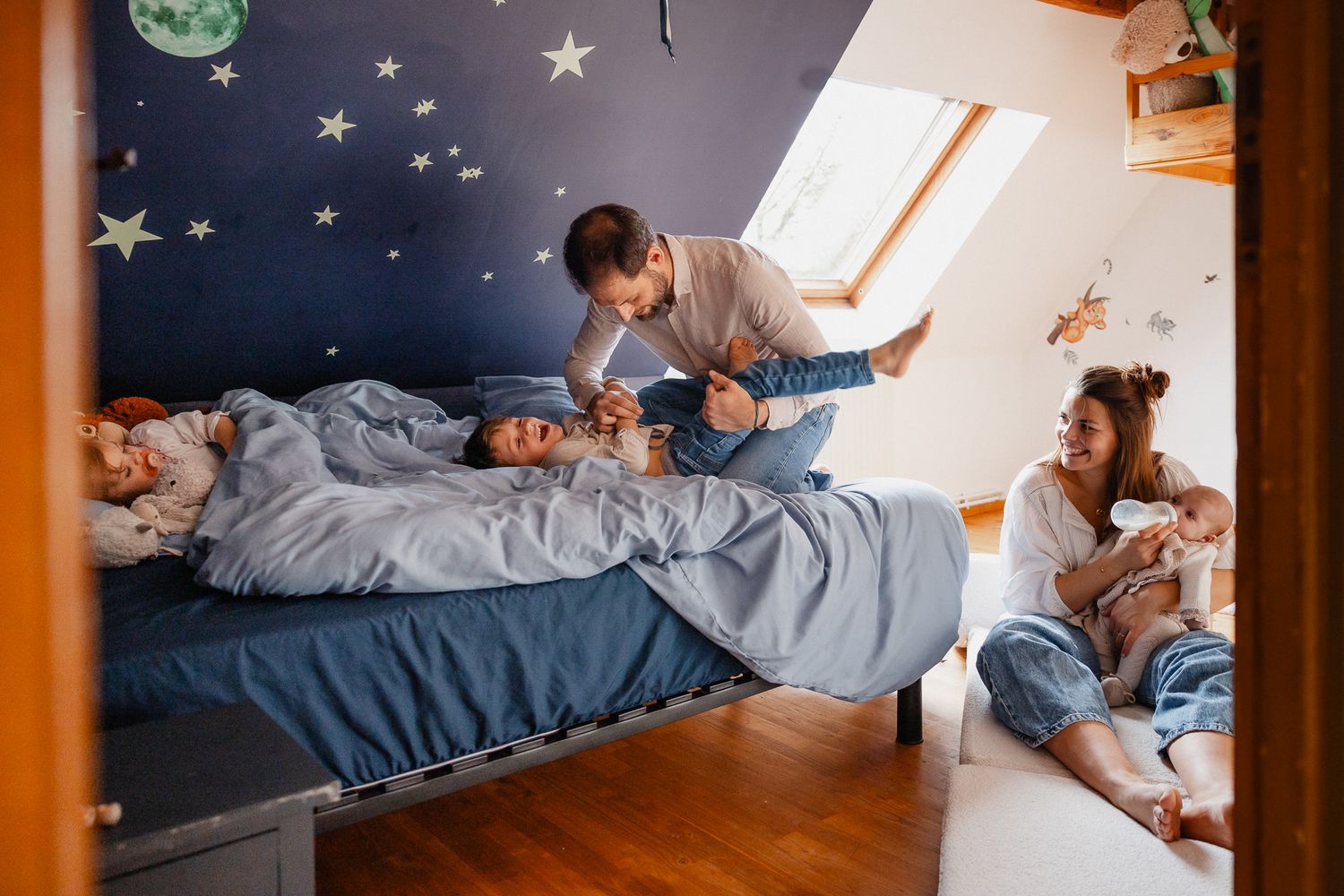 Vie de famille capturee en seance photo a domicile a Lille, le bebe boit son biberon, le grand joue avec son papa, la deuxieme sieste