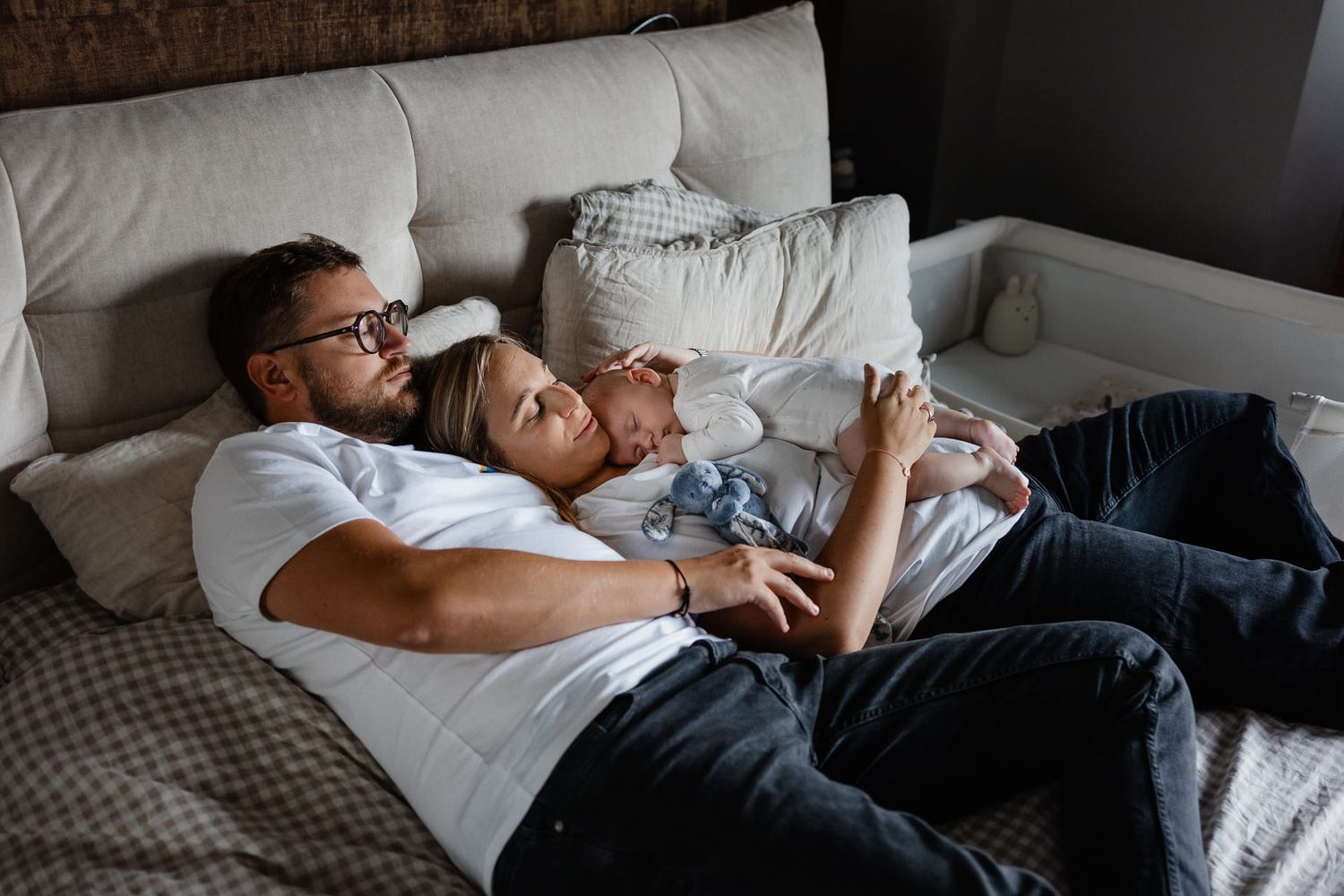Photographe naissance lifestyle Lille, nouveau-ne endormi tendrement dans les bras de ses parents sur le lit de la chambre