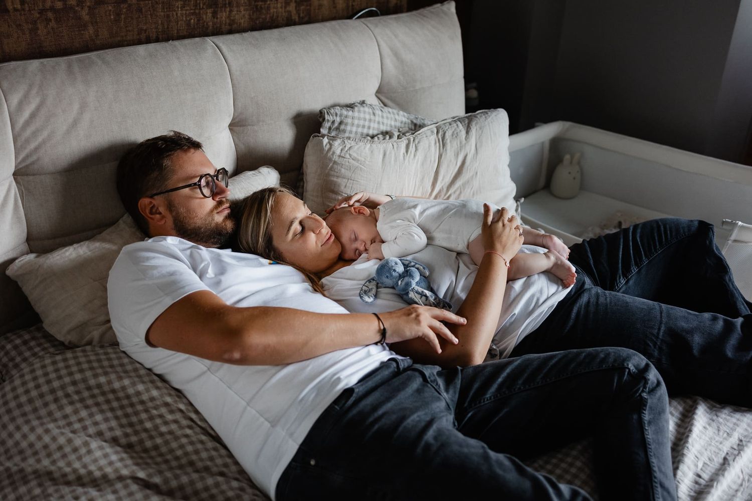 Photographe naissance lifestyle Lille, nouveau-ne endormi tendrement dans les bras de ses parents sur le lit de la chambre