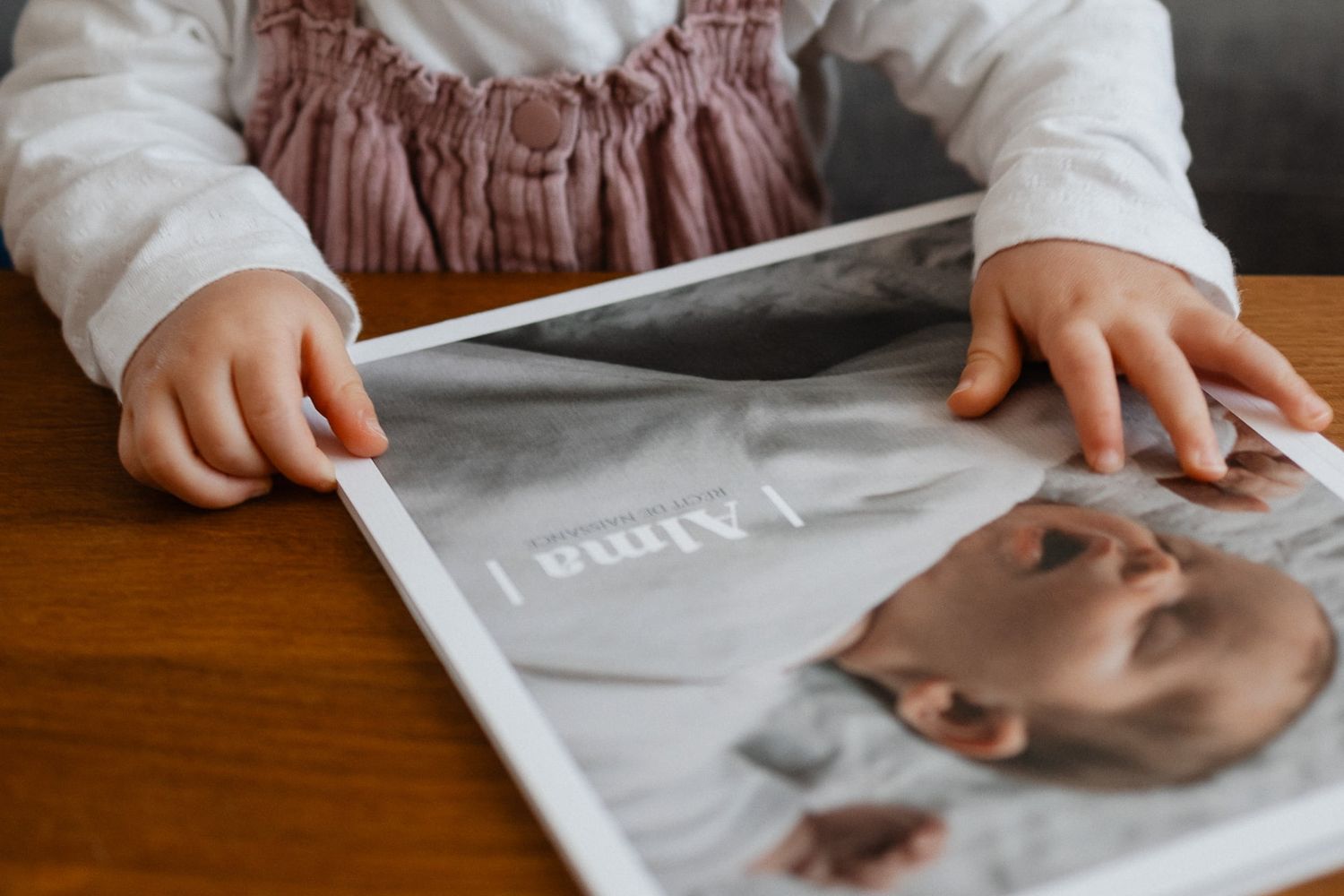 Petites mains d'un enfant decouvrant son livre de naissance cree avec les joues roses atelier par une photographe famille de Lille