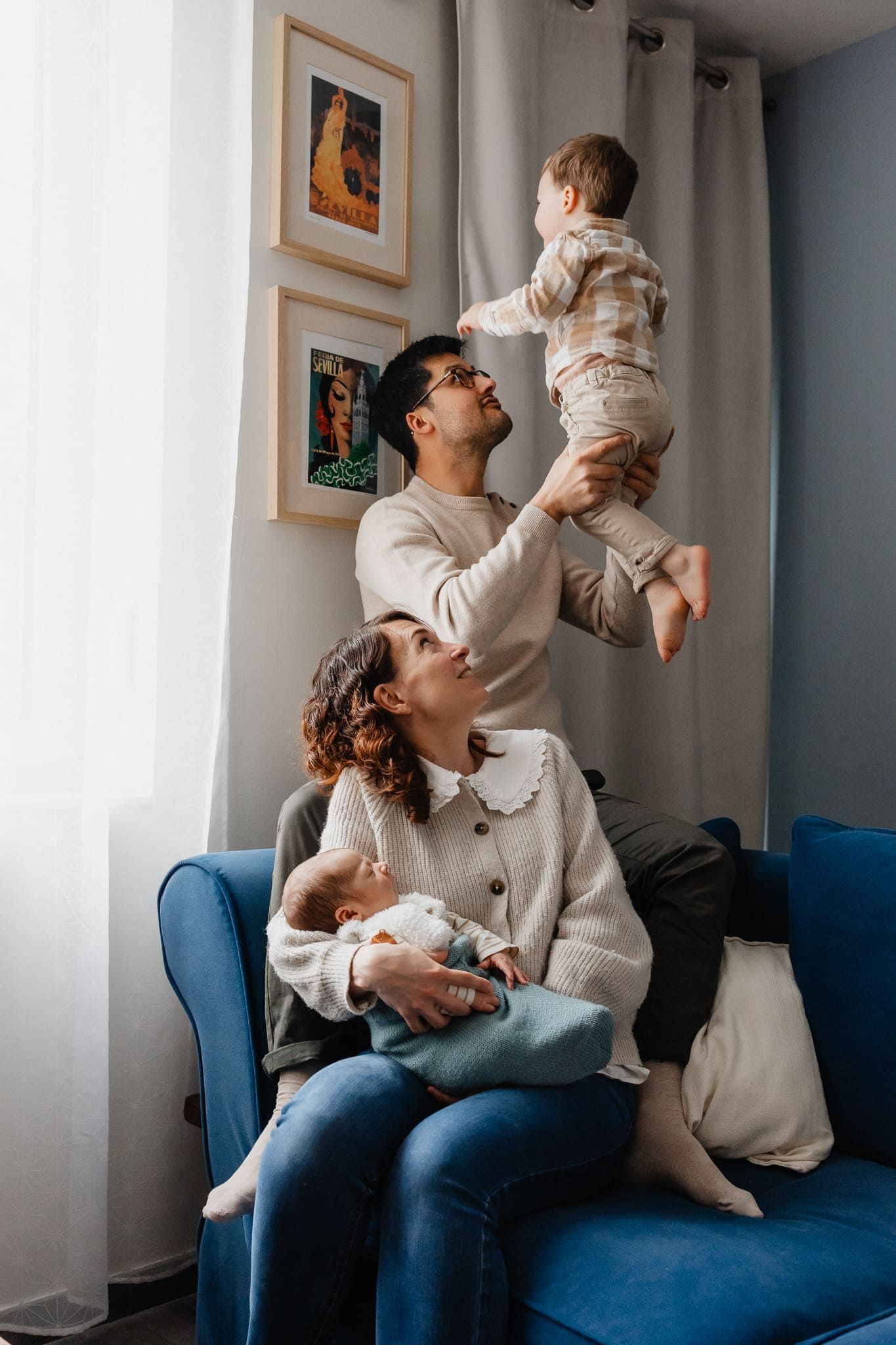 Papa fait voltiger son fils sur le canape sous le regard de maman calinant bebe en seance photo de famille a Marcq en Baroeul pres de Lille