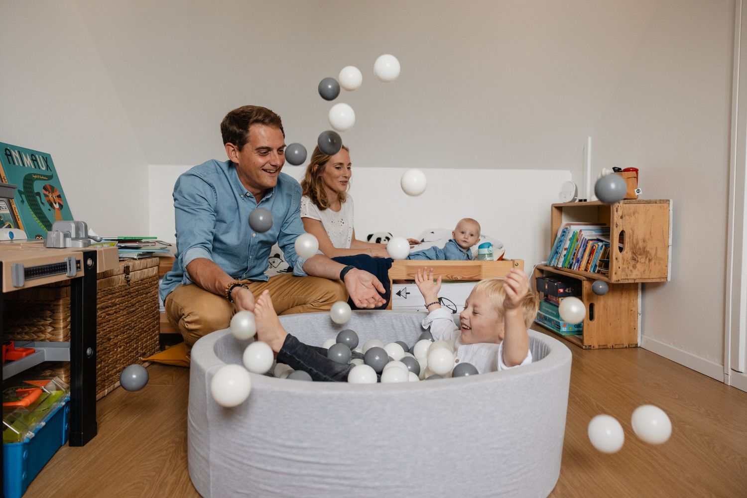 Famille joyeuse dans la chambre des enfants jouant dans la piscine a balles pendant une seance photo naissance en famille a domicile a Lille