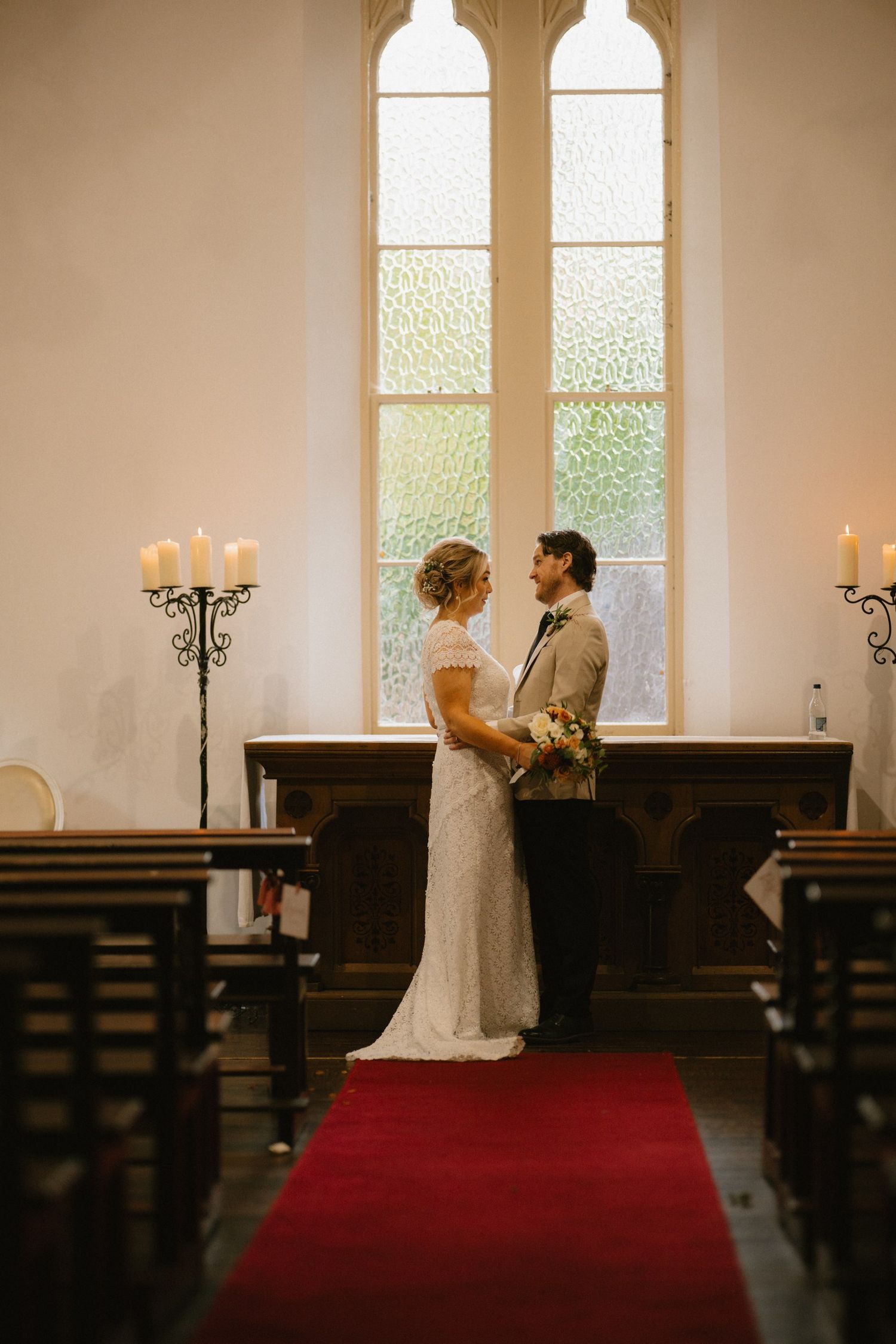 Bride and groom beside the tall chapel window at BrookLodge and Macreddin Village.