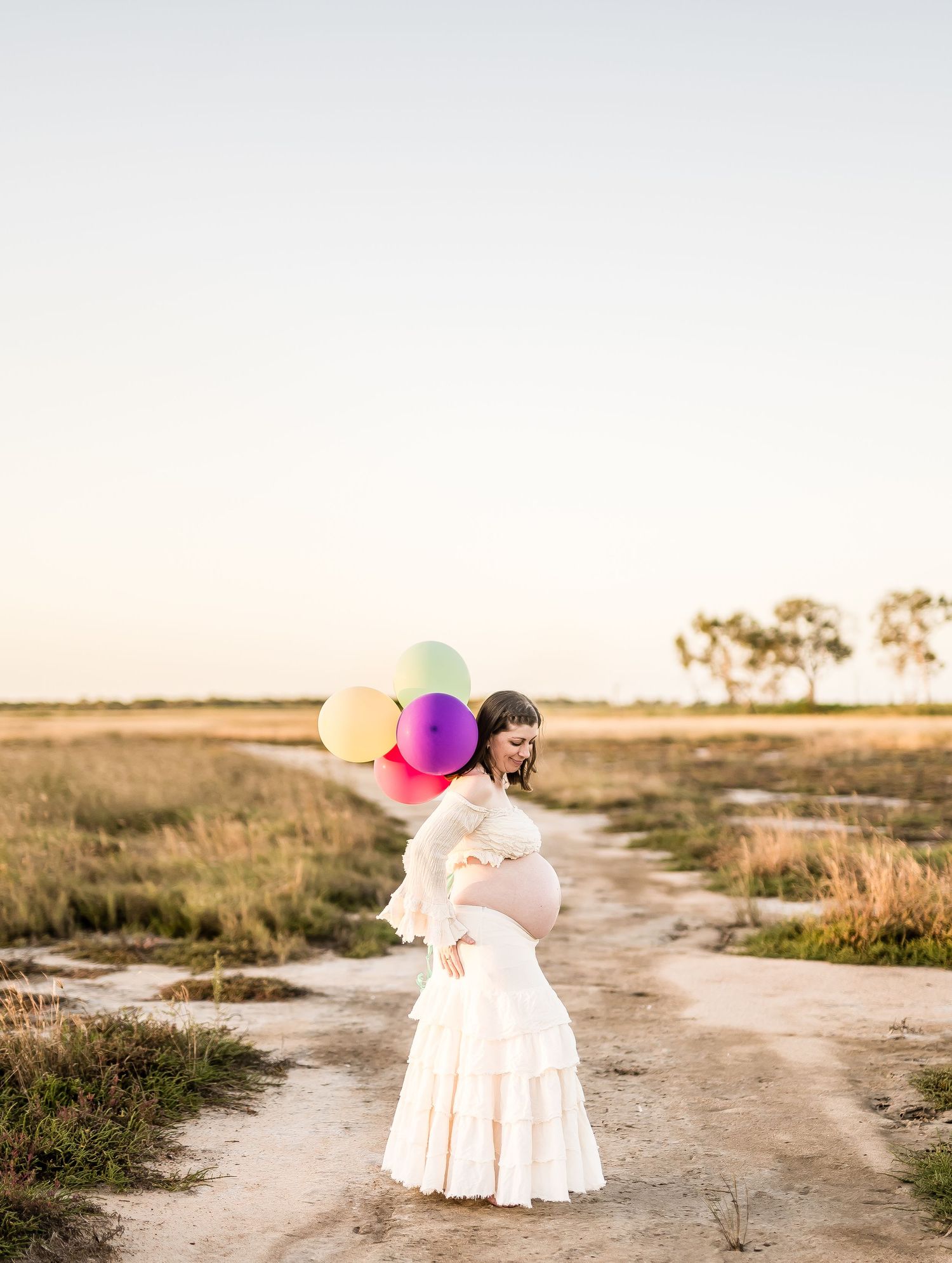 Dreamy sunset portrait session featuring colorful balloons and flowy dress in an open field.