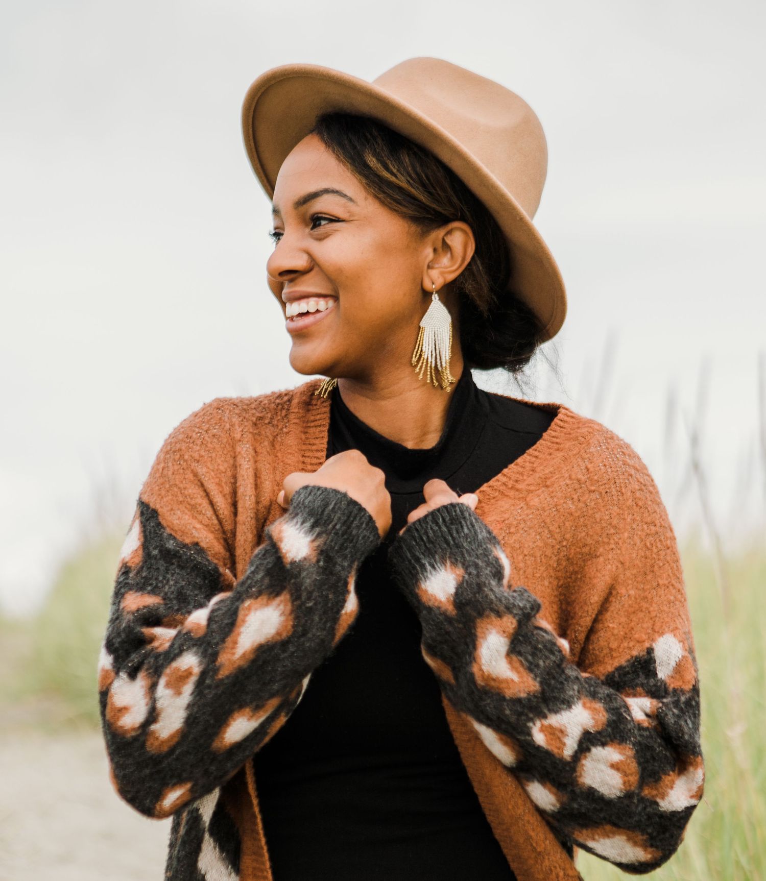 Stylish woman in leopard print cardigan and tan fedora hat smiling outdoors in natural light.
