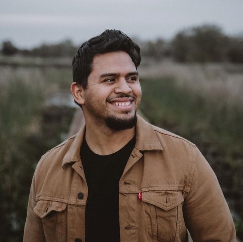 Smiling young man wearing a brown Levi denim jacket and black shirt photographed outdoors.
