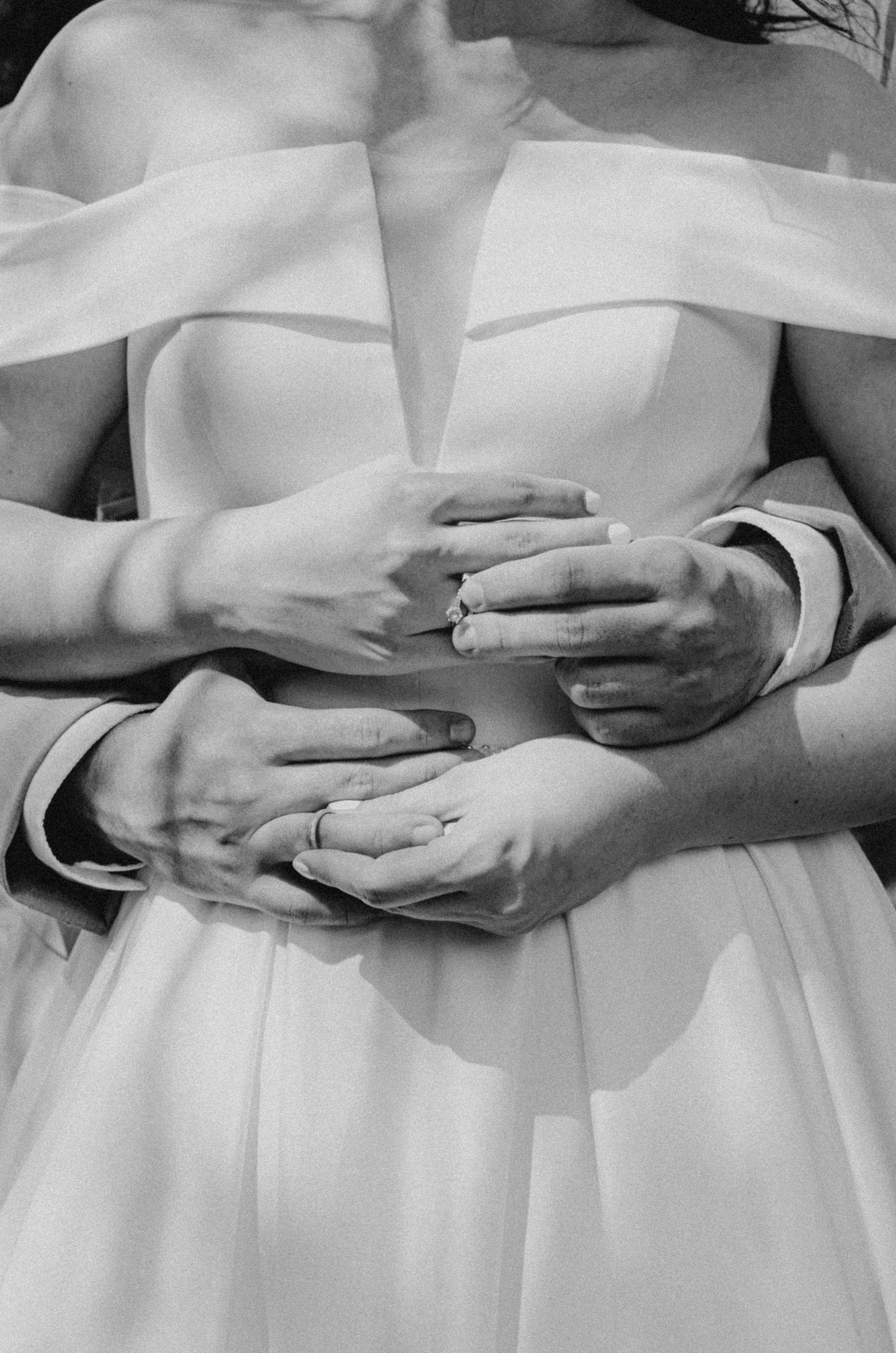 Close up of newlyweds' hands showing wedding rings against a white wedding dress.