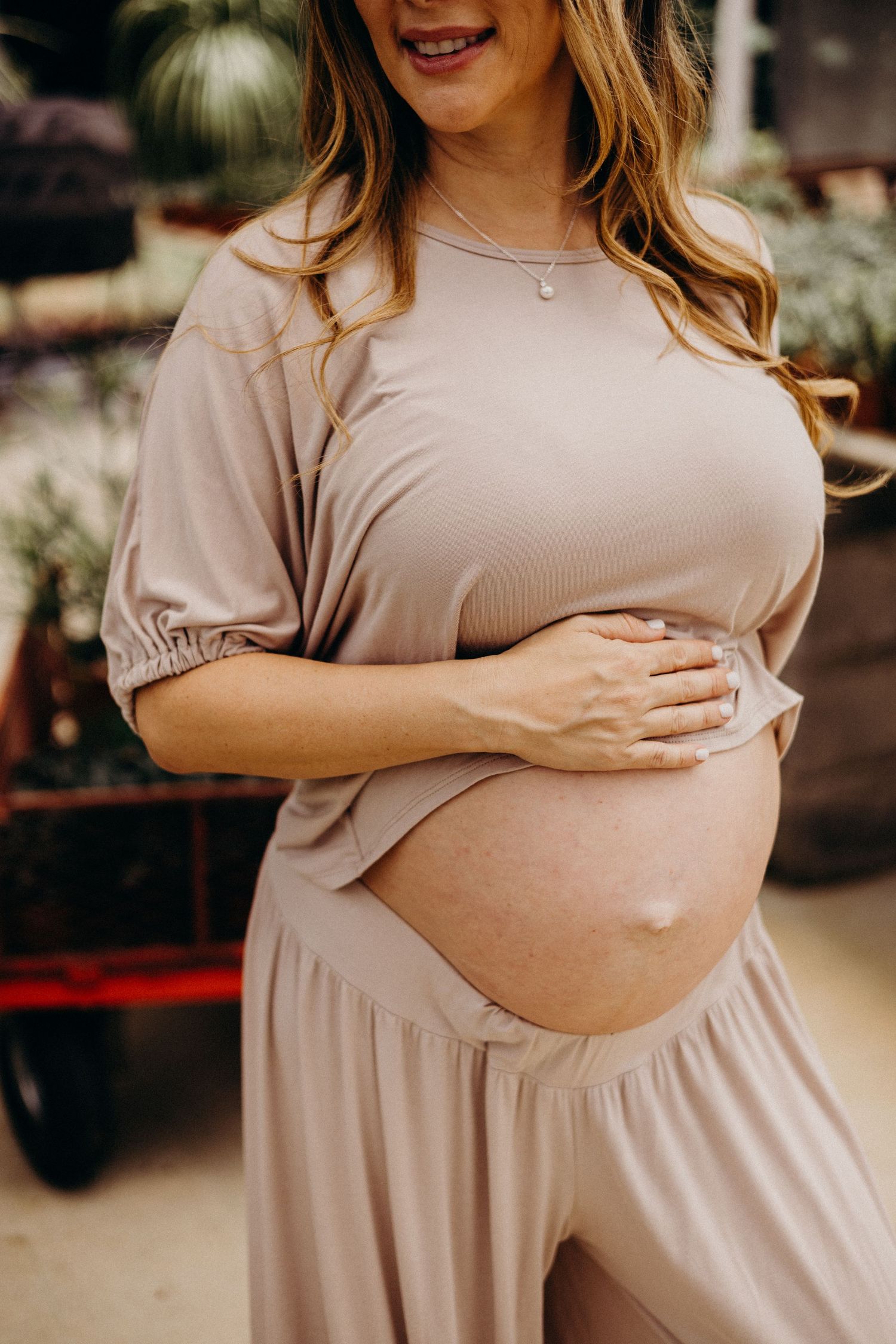 A pregnant woman in a beige dress cradles her baby bump in a series of maternity photos.