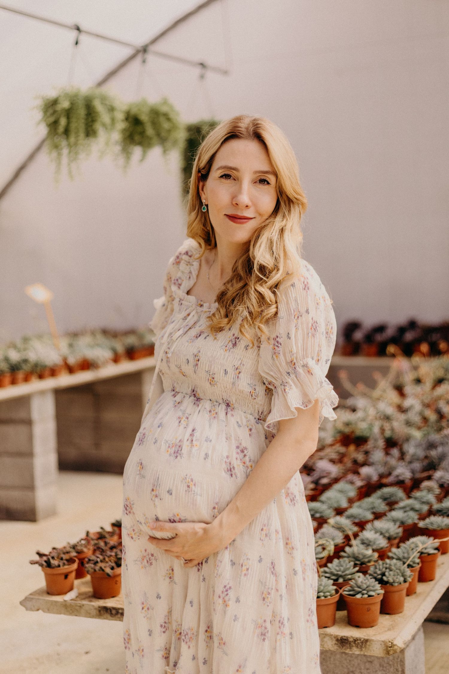 A floral dress in a greenhouse setting with rows of potted succulent plants and hanging greenery.