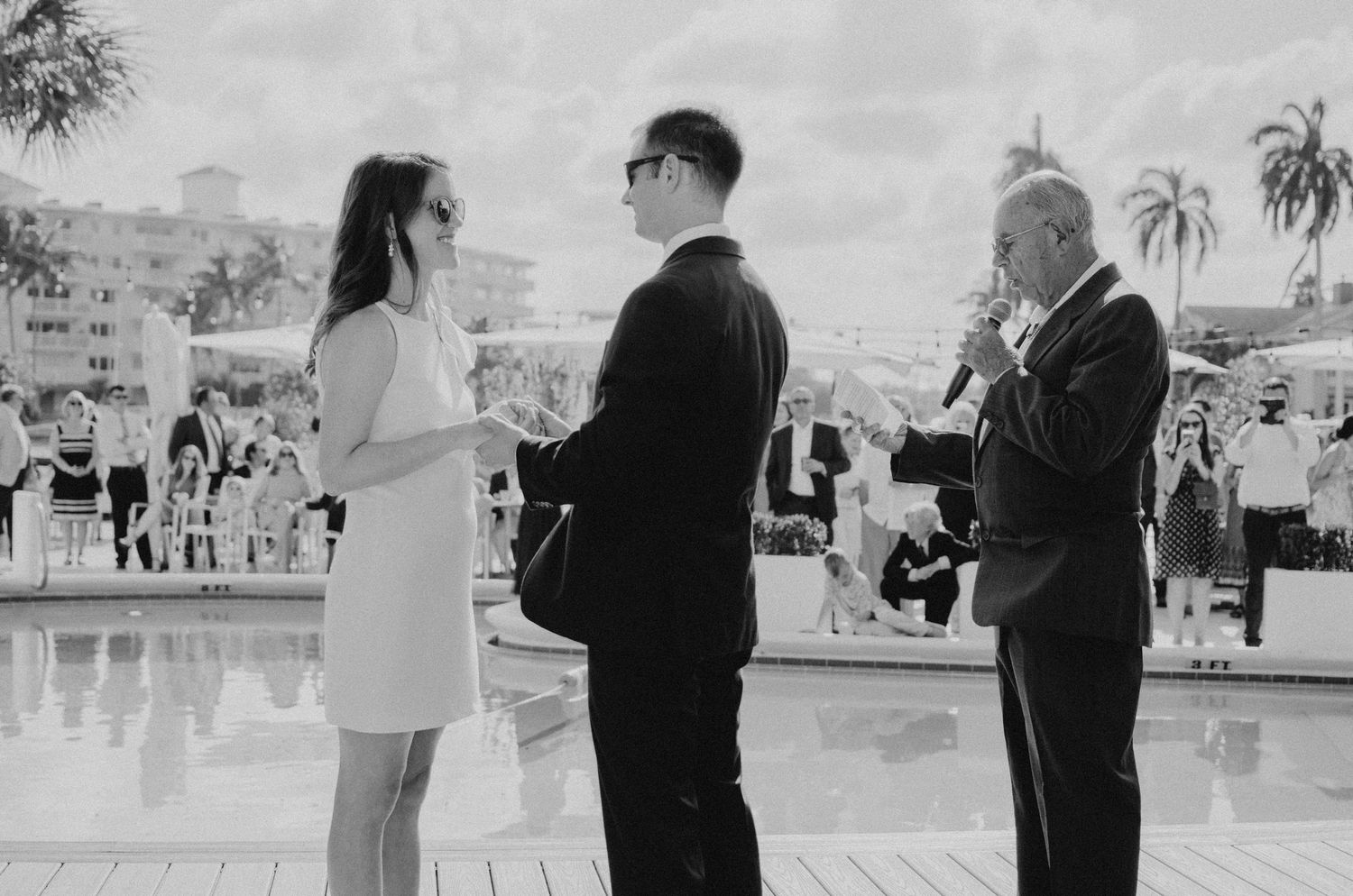 A wedding ceremony on an outdoor patio with palm trees in the background.