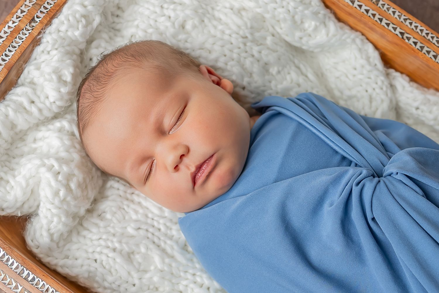 Sleeping baby wearing blue clothing rests peacefully on soft white blanket.