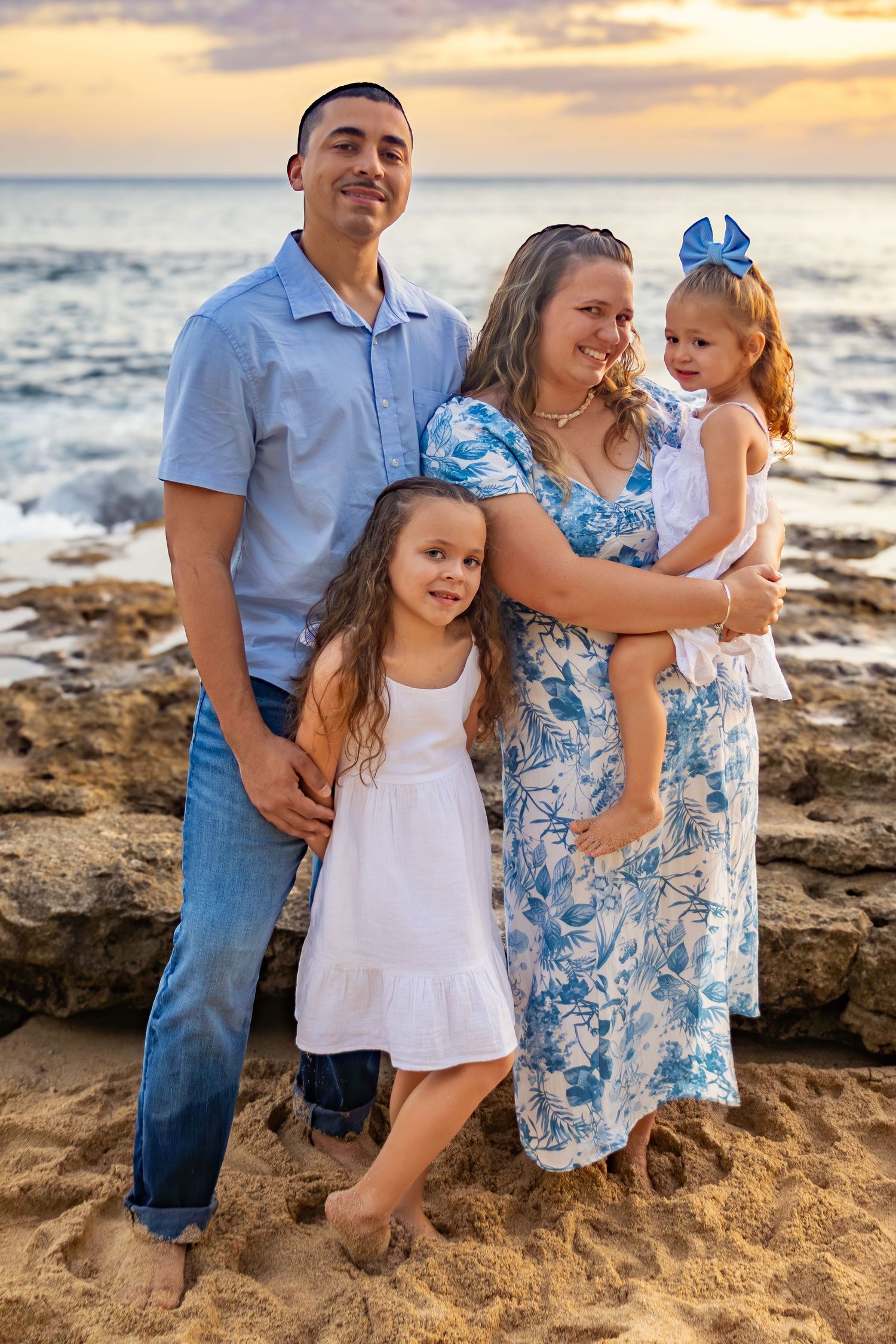 A family portrait on a rocky beach at sunset wearing coordinated blue and white outfits.