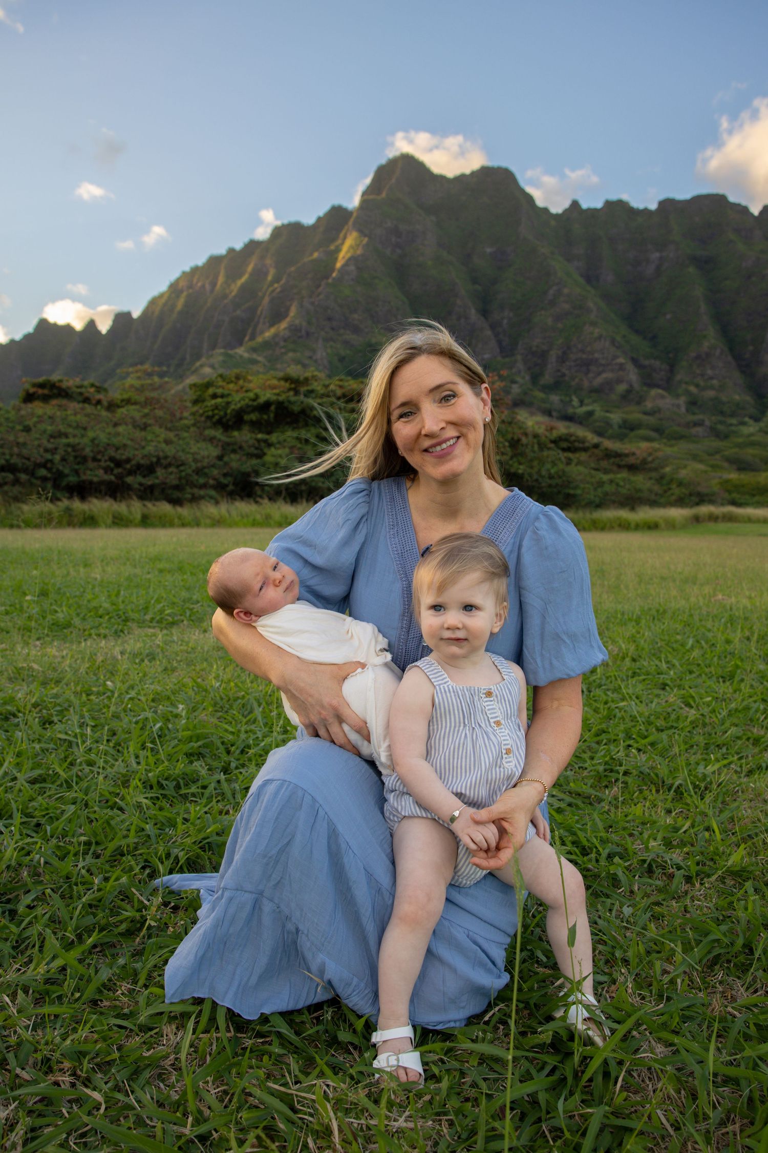 Family group sitting together on grass with dramatic mountain peaks in background.