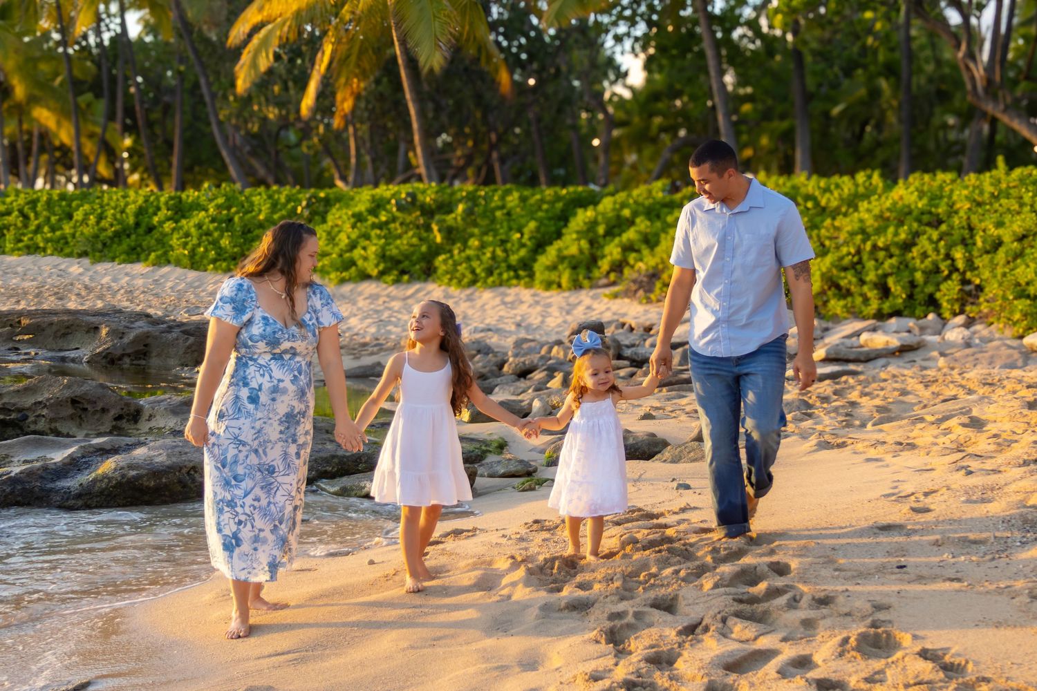 A family walks together along a beautiful beach at sunset with palm trees in the background.