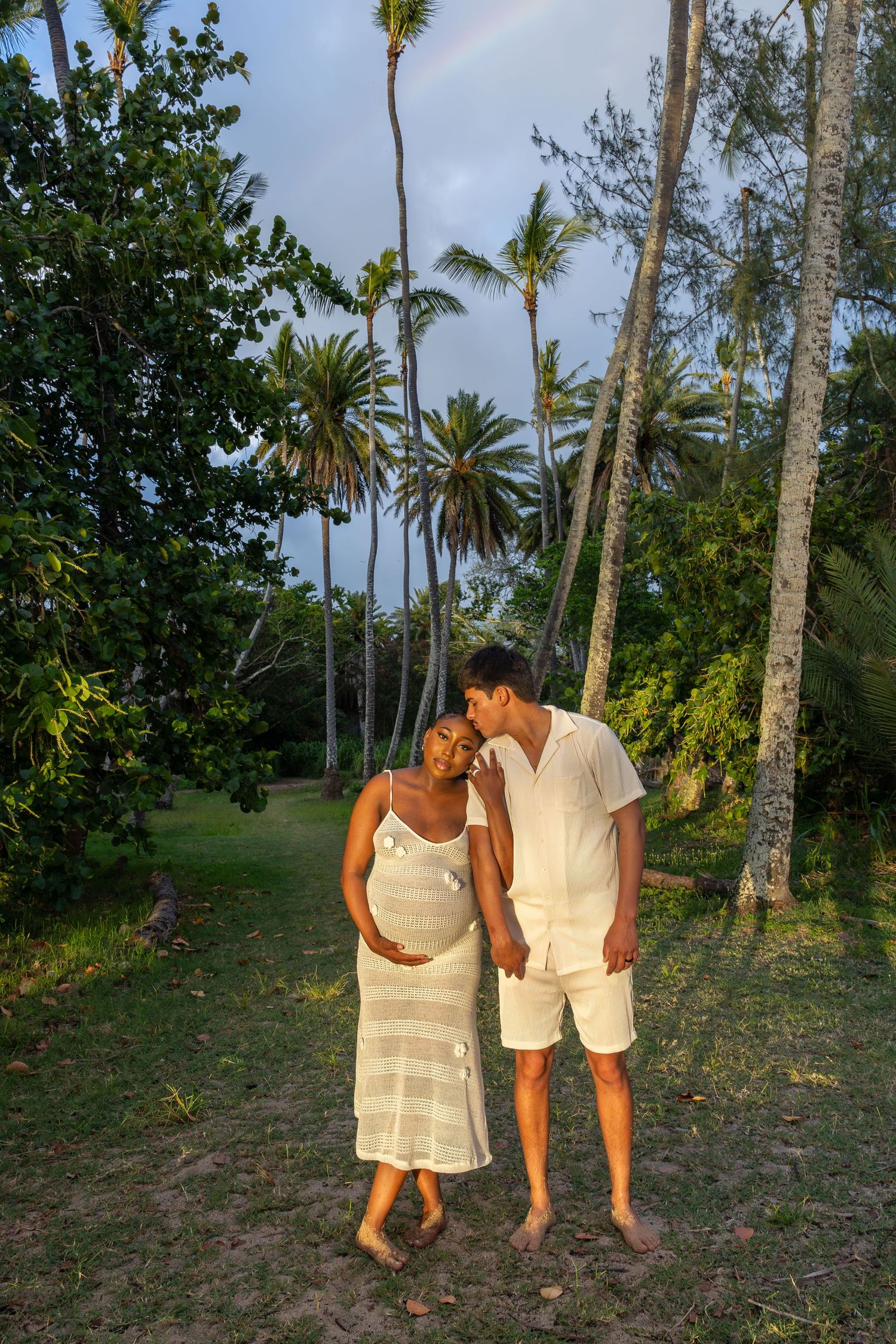A romantic couple walking together among palm trees in a tropical setting at sunset.