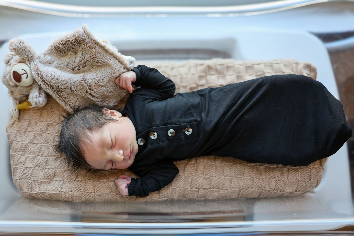 A sleeping baby in black outfit rests on a textured beige blanket.
