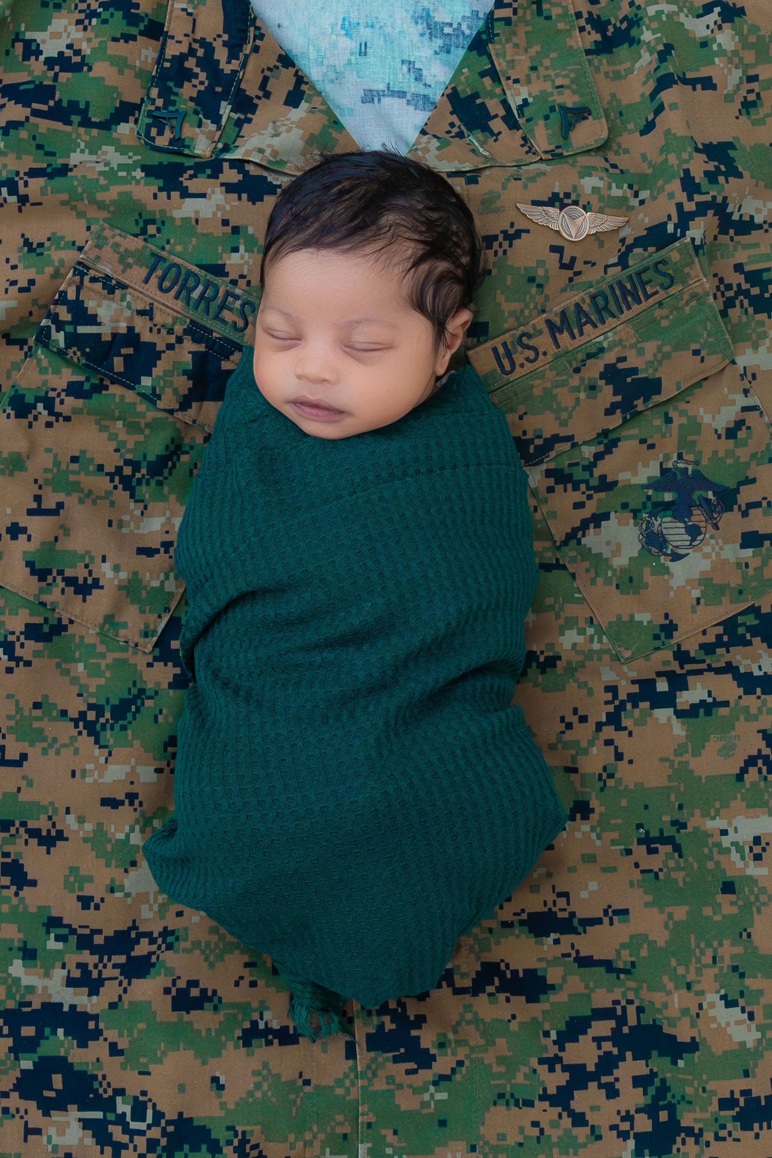 Sleeping newborn swaddled in green blanket on military camouflage background.