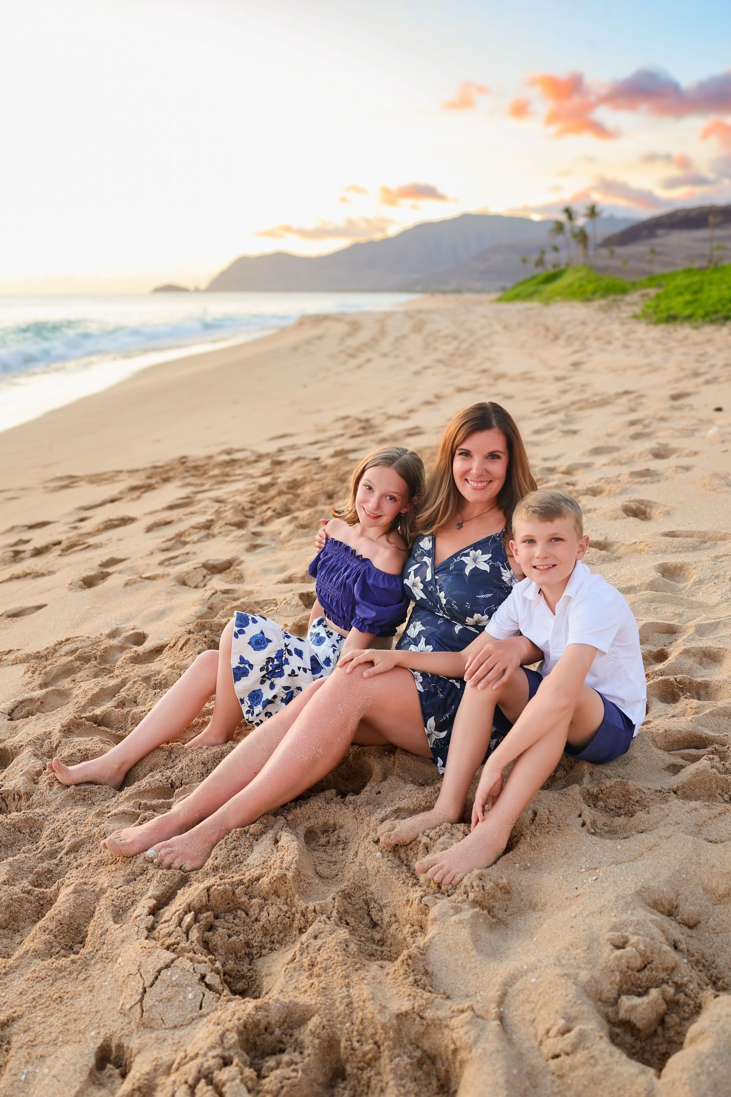 Beach portrait at sunset with three people sitting together on sandy shore.