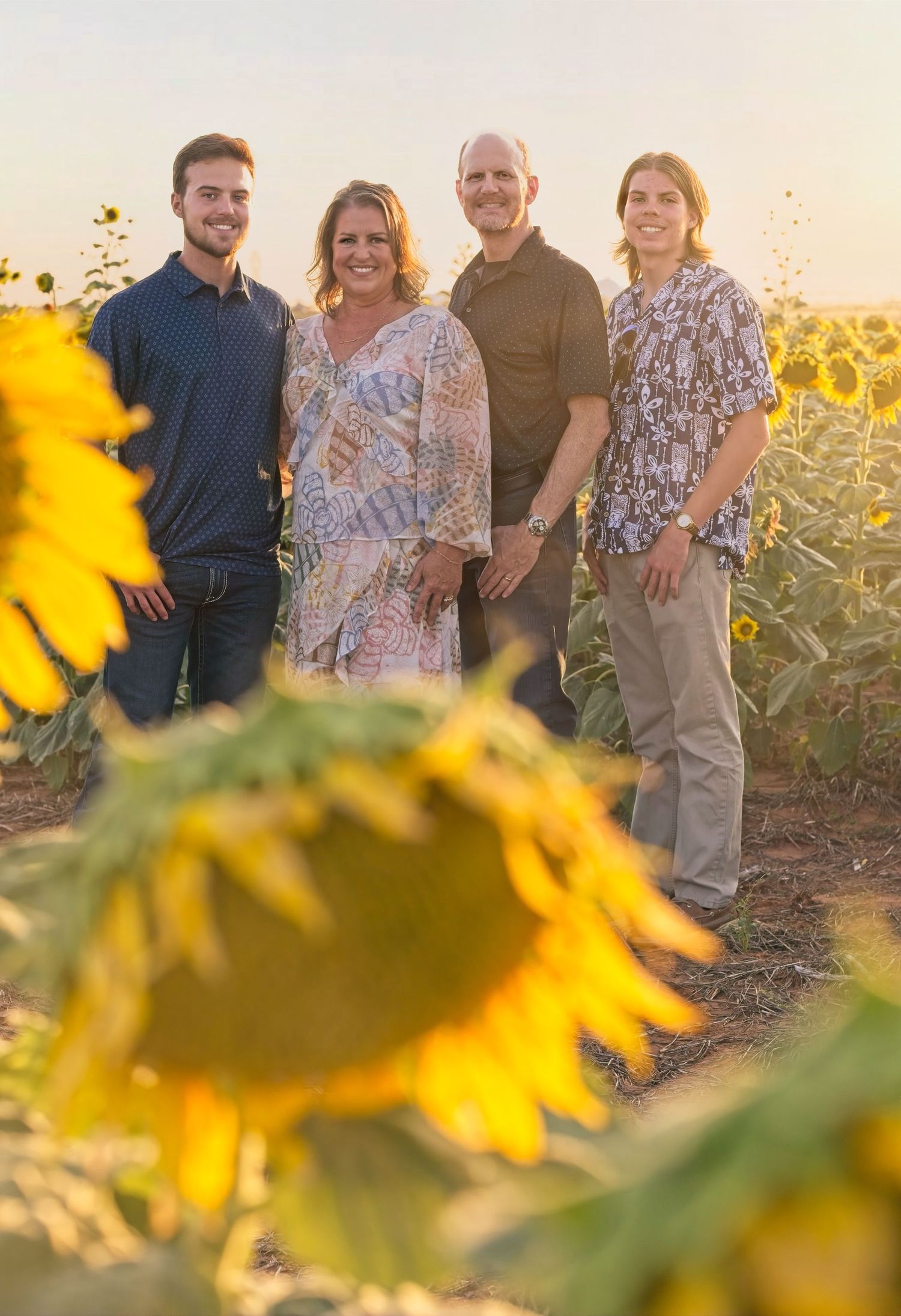 Four people pose together in a sunflower field during golden hour sunset.