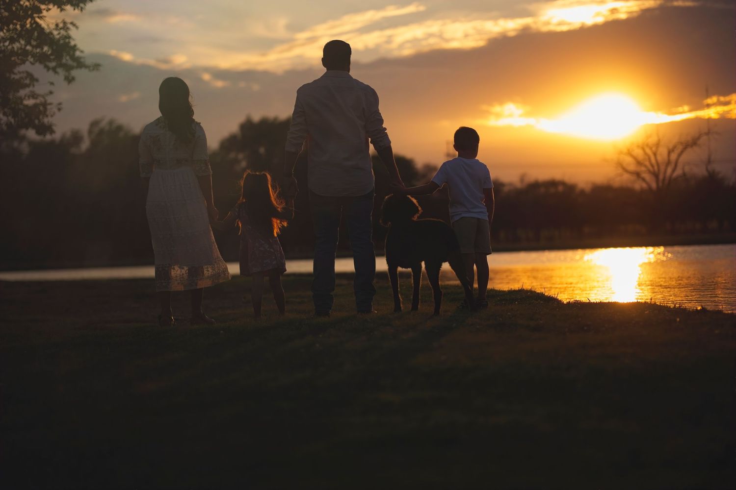 Silhouettes of people watching a vibrant orange sunset over water.