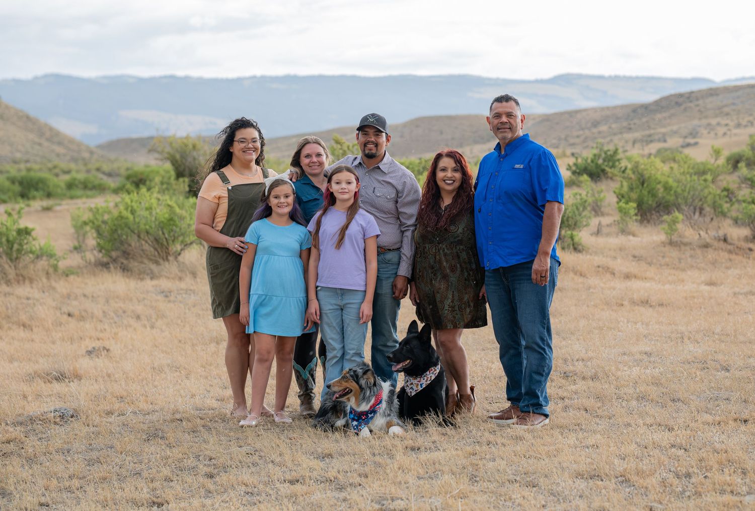 Family group portrait with two adults, four children, and a dog posing outdoors in a scenic desert landscape.