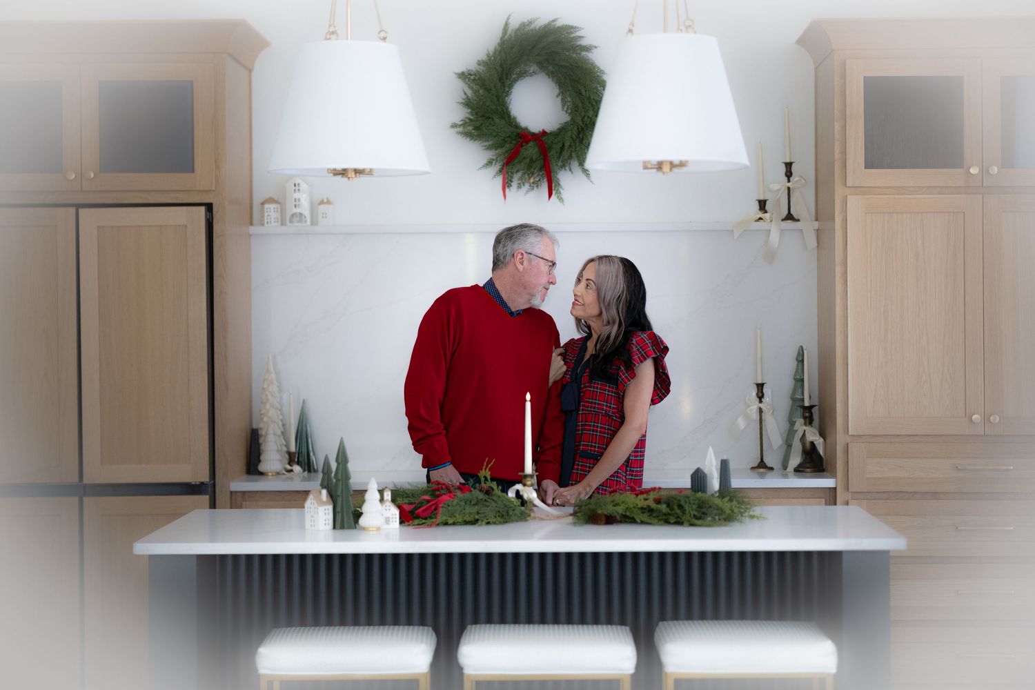 Holiday decorations and greenery adorn a white kitchen counter with wall sconces and cabinets.