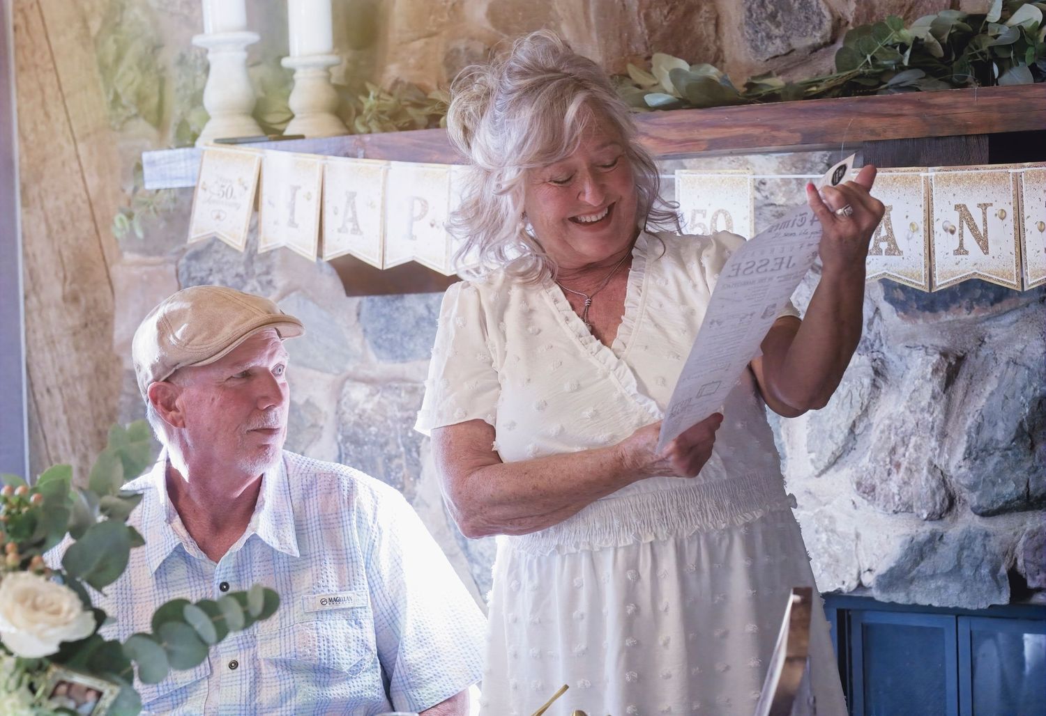 Two people in white outfits sitting together in a rustic outdoor setting.