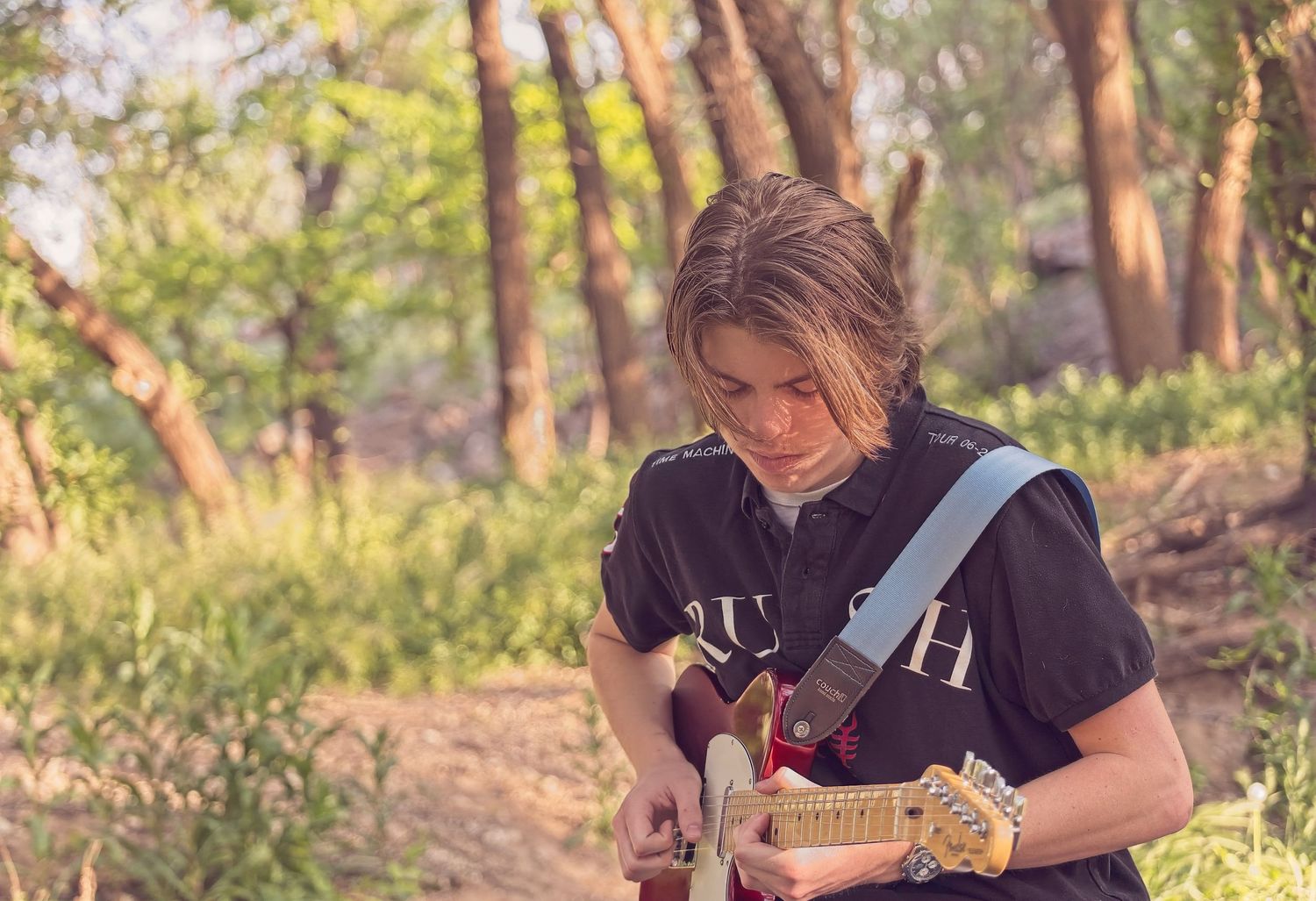 Musician playing electric guitar outdoors in natural lighting.