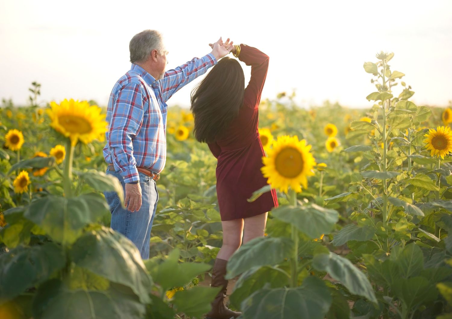 Two people dance together in a beautiful sunflower field at sunset creating a romantic summer moment.