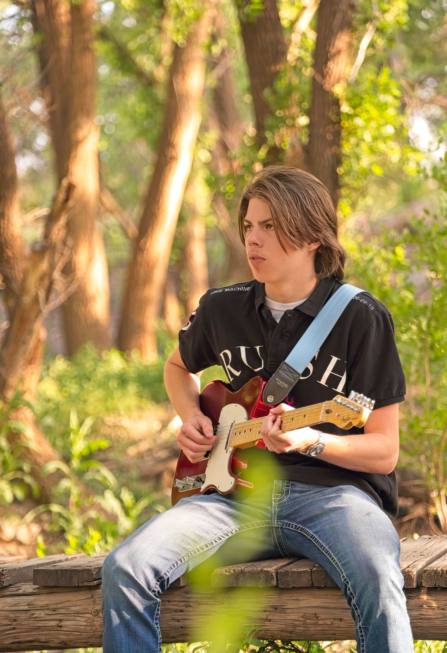 Guitarist playing electric guitar while sitting on log in sunlit forest.