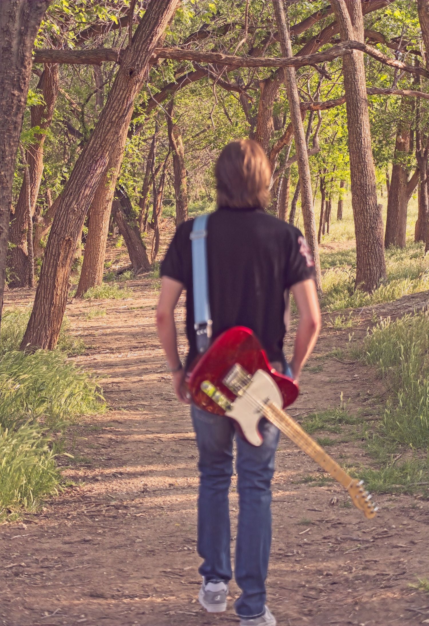 Person walking on forest path carrying red electric guitar.