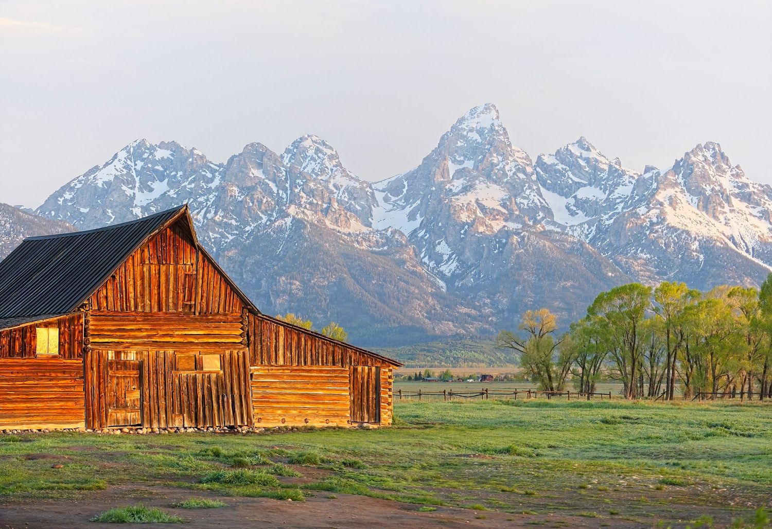 Historic wooden barn beneath the majestic Grand Teton mountains at sunrise.